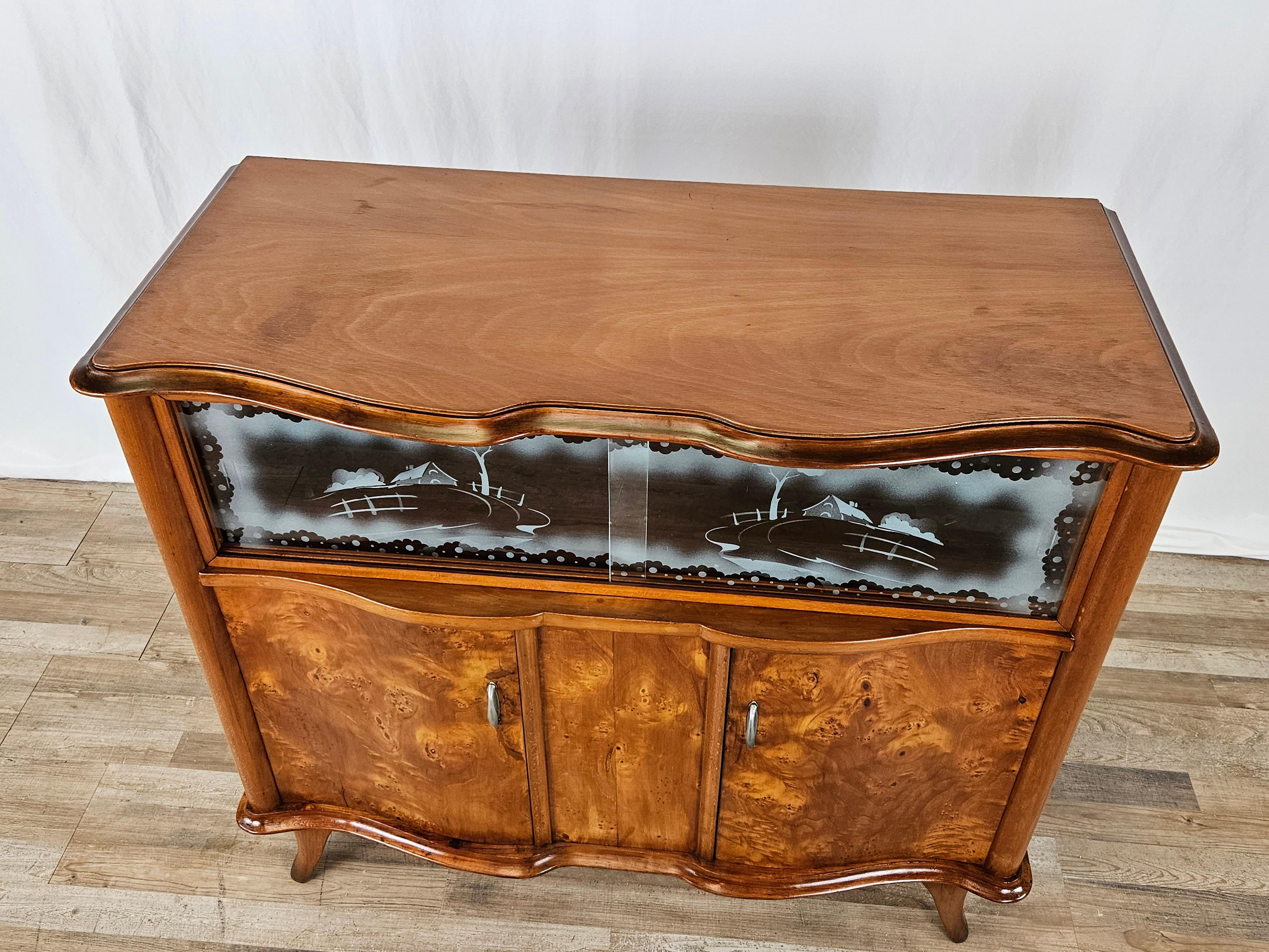 Small sideboard or cabinet in blond walnut burl, mid-20th century Italian manufacture.

Refined and lively, it features a double door with a single internal compartment.
Two sliding glass panes with frosted decorations covering an additional