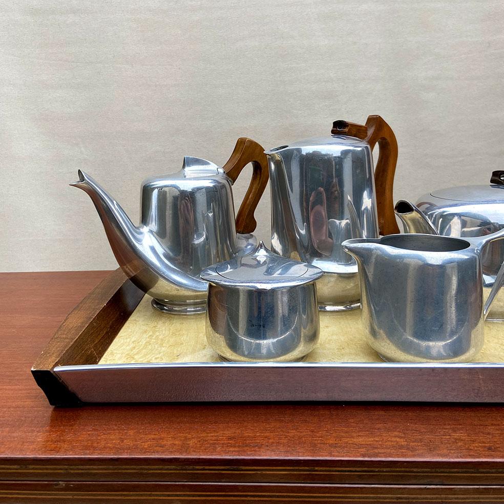 Picquot-ware 1960s Tea and Coffee 5-Piece Set with tray by Burrage & Boyde.

British, 1960s 
Made from Aluminium with Sycamore wood details. Tray is a combination of these 2 materials with a formica base.

Price is for the complete set of 5 with