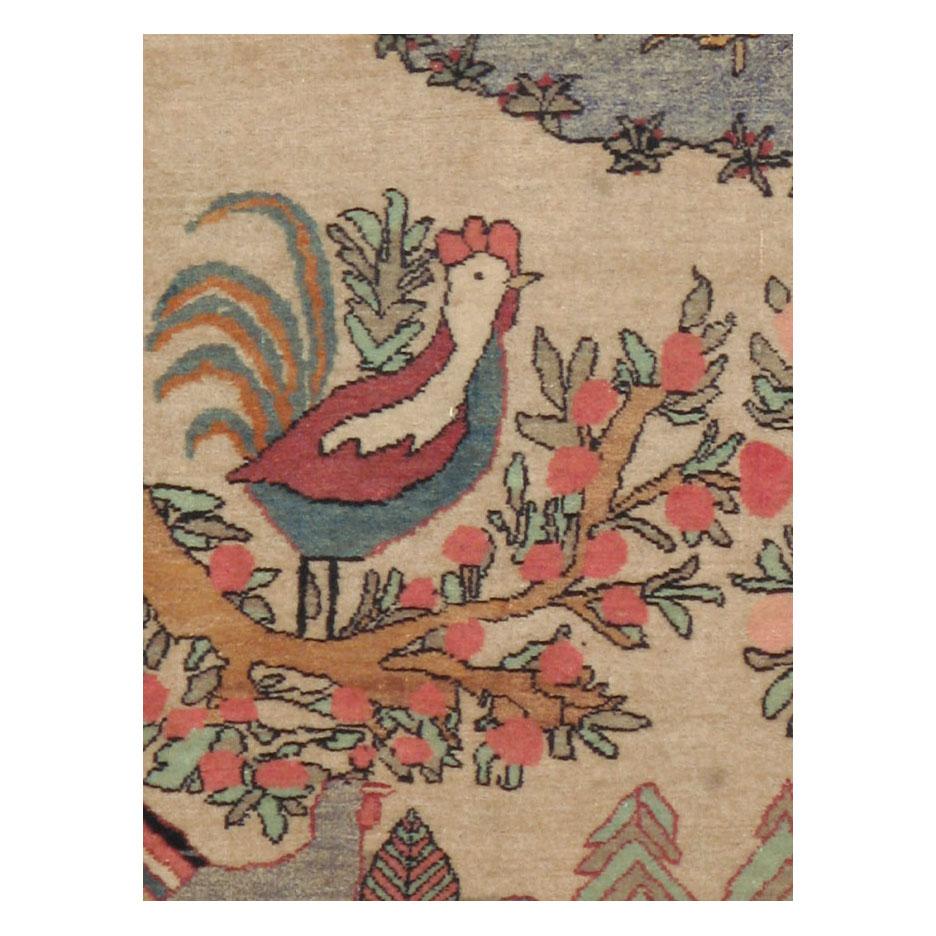 A vintage Persian Mashad accent rug handmade during the mid-20th century. The pictorial design consists of a large tree with birds perched among 2 cypress trees centered in front of the seafoam blue sky. Various animals including a peacock, rooster,