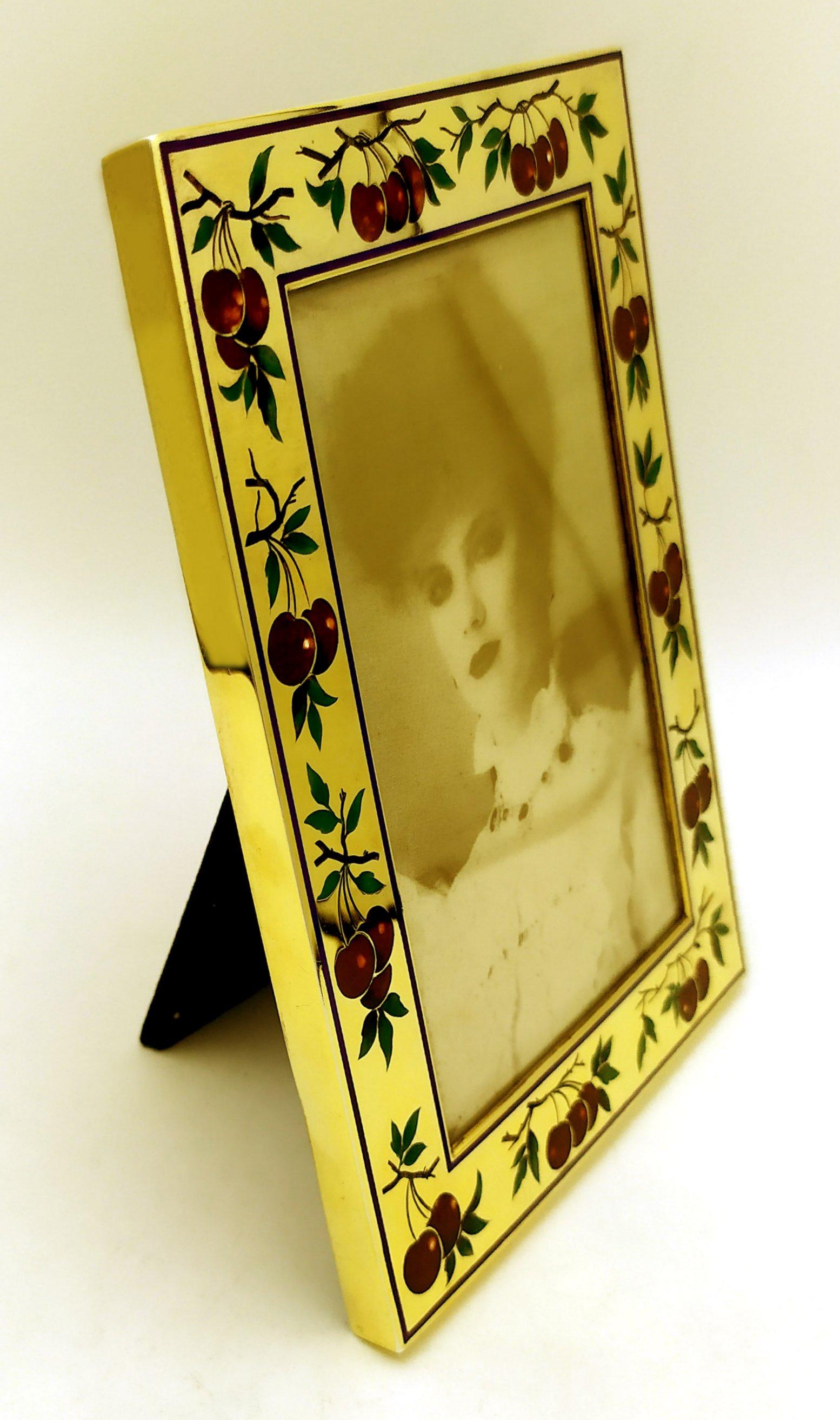 Rectangular photo frame in gold plated 925/1000 sterling silver with fine engraving of fruit (cherries) fire enamelled with polychrome colours, contemporary style. Ground glass and alcantara back panel. External measurements cm. 13 x 17, internal