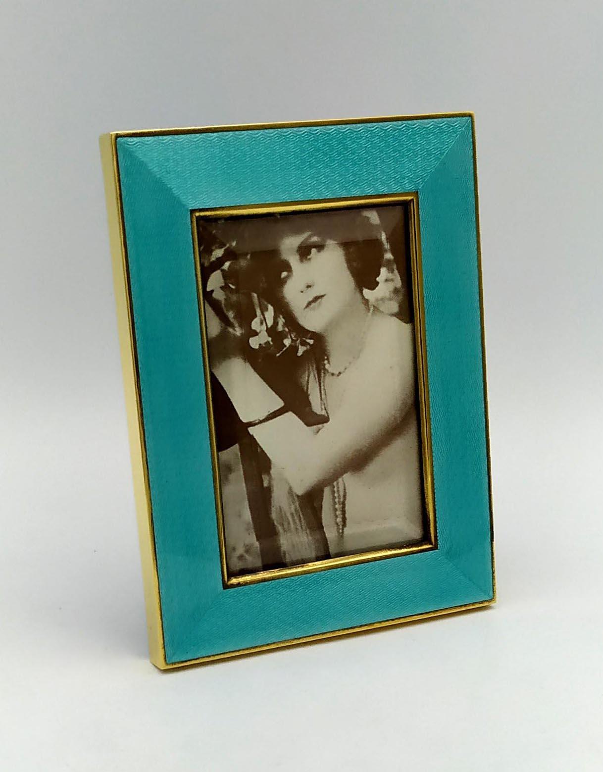 Cornice portafotografie rettangolare in argento 9251000 dorato con smalto traslucido a fuoco su guillochè. Stile moderno contemporaneo. Vetro molato. Pannello in velluto blu. Dimensioni esterne cm. 10 x 13, interne cm. 6 x 9. Peso gr. 136. Disegnata