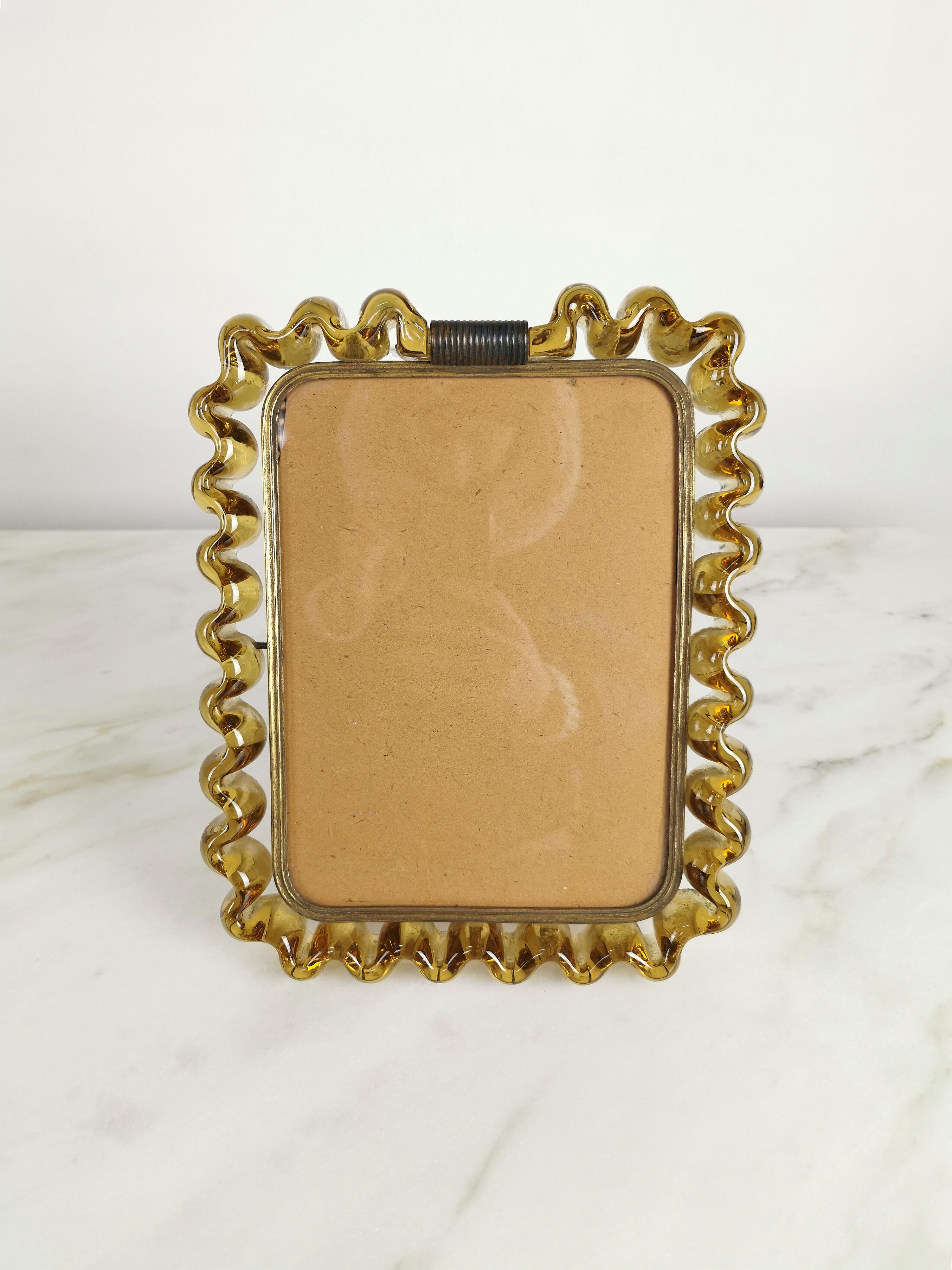 Rare and elegant Venini photo frame of considerable size, produced in Italy in the 1940s.
The photo frame was made in Murano glass with a ribbon in the shade of amber with structure and accessories in brass.