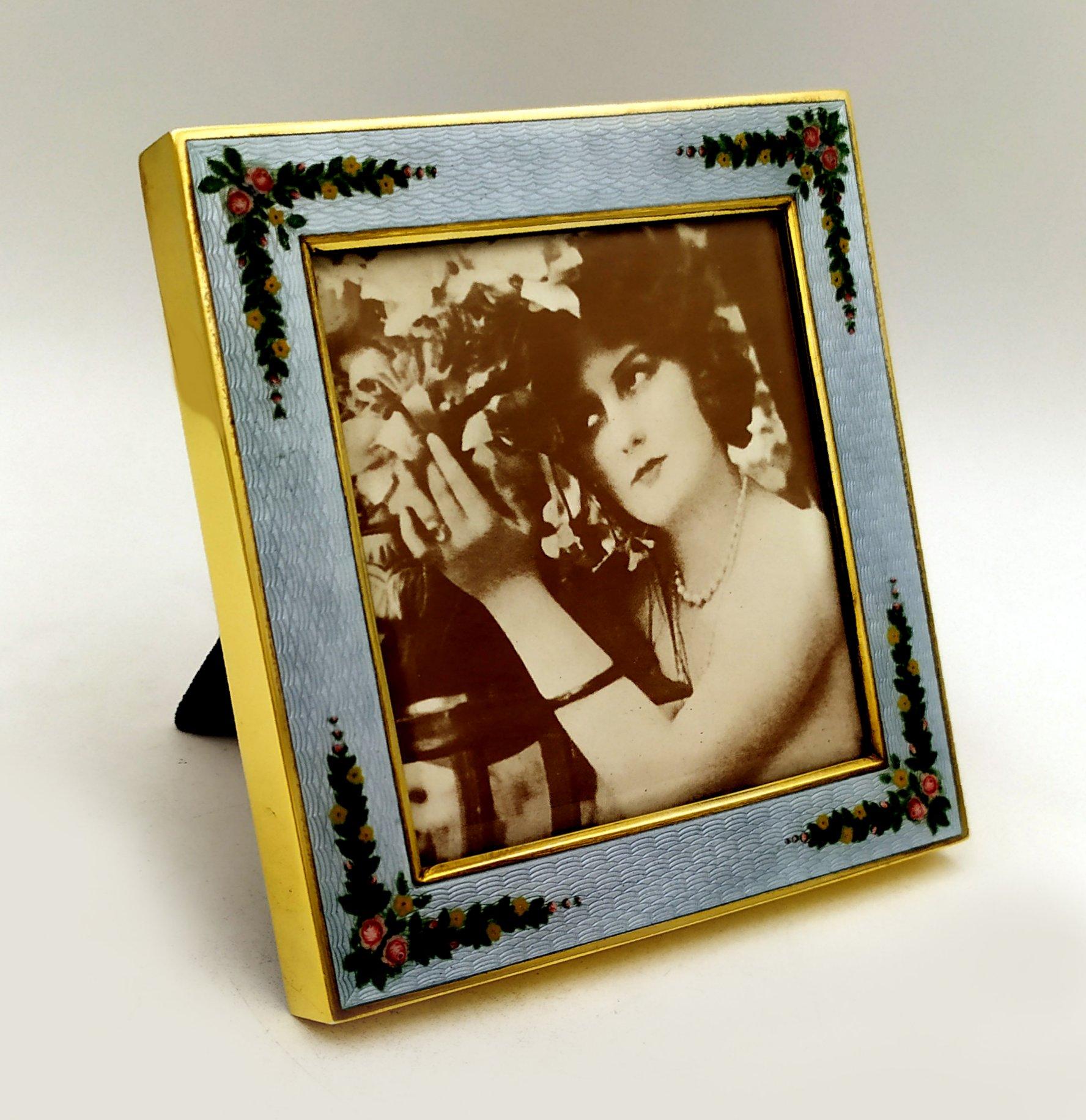 Portafoto quadrato in argento 925/1000 placcato oro con smalto grigio perla traslucido cotto a guilloché e miniatura dipinta a mano di ghirlande di fiori in stile Art Nouveau viennese della fine del XIX secolo. Misure esterne cm. 10,8 x 10,8 Misure