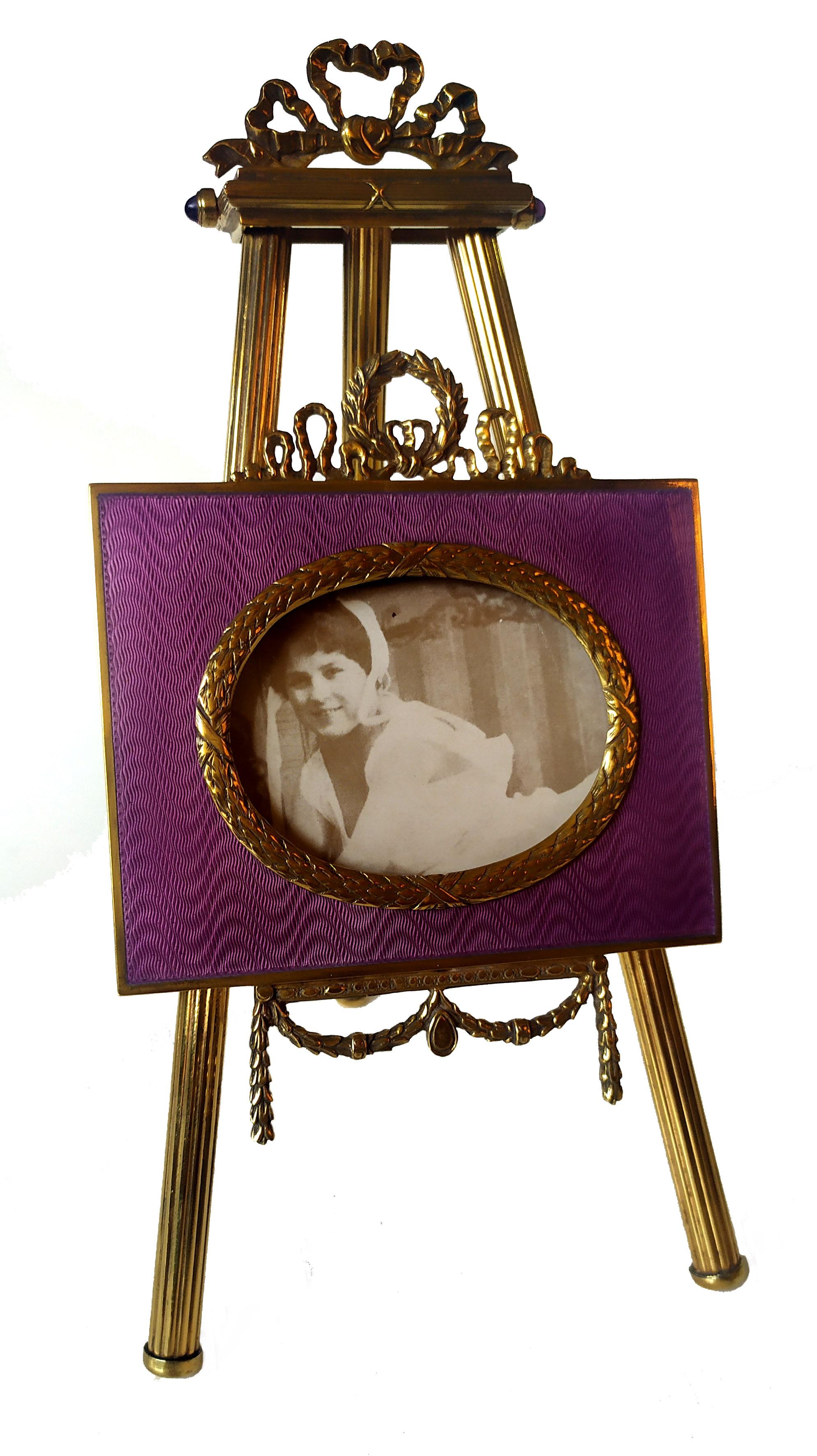 Photo frame mounted on easel like tripod of striped tubings, in 925/1000 sterling silver gold plated with translucent fire enamel on guillochè. Russian Empire style ornaments late 19th, early 20th century. Oval photo cm. 5.5 x 7. Outer dimensions