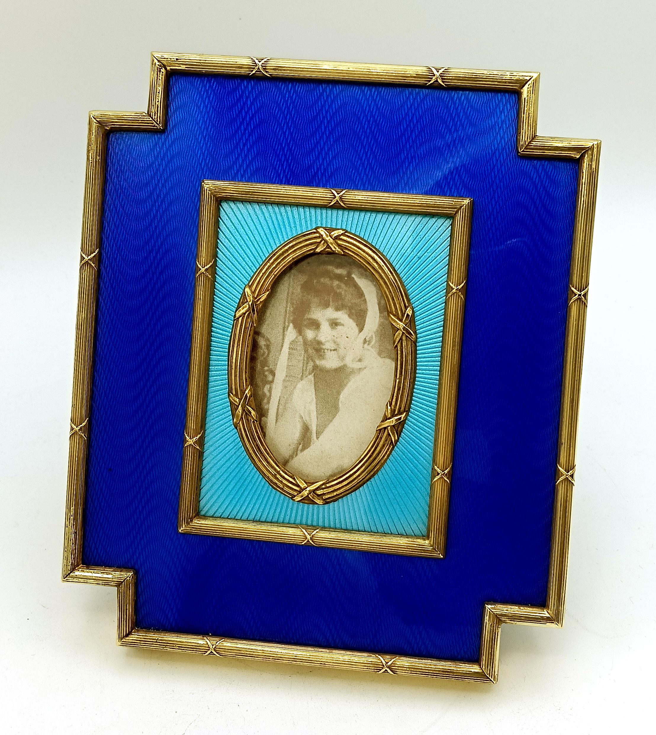 Cadre extérieur rectangulaire avec angles rentrants pour photo ovale, en argent sterling plaqué or 925/1000 avec émail translucide bicolore sur guillochage. Bordures et ornements de style Empire français Louis XVI. Panneau en alcantara bleu.