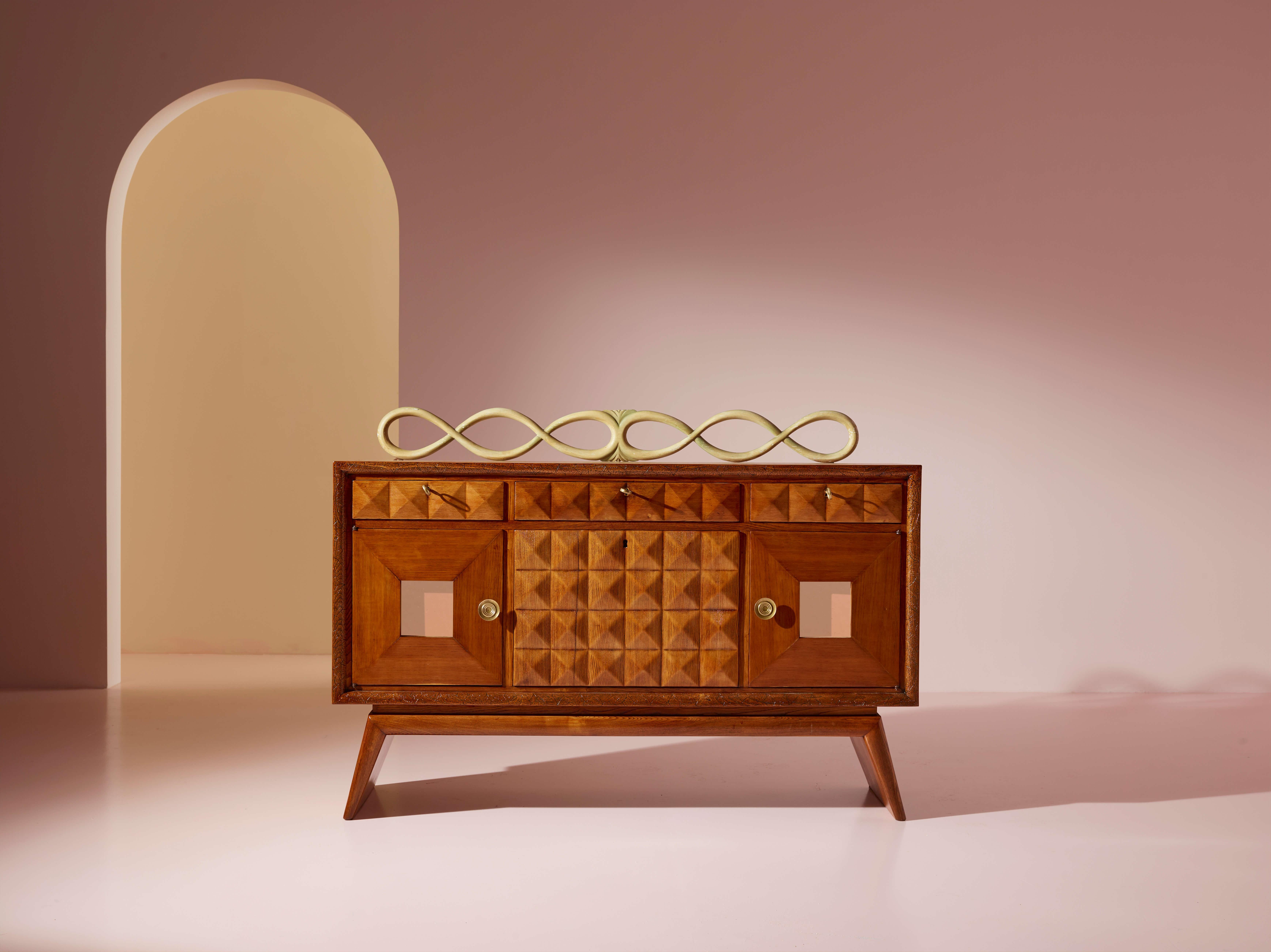 Italian oak sideboard with mirrored inserts, sculpted and lacquered cornice, manufactured by Pierluigi Colli, 1940s

This small Italian oak cupboard holds a delightful secret. Lowering the central drop-down door reveals a mirrored bar compartment, a