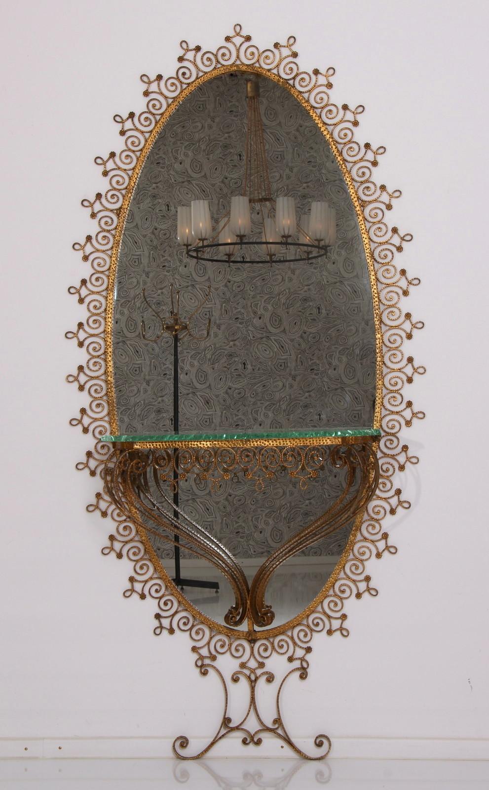 Miroir de sol en fer forgé doré fait à la main avec son verre miroir d'origine, conçu par Pier Luigi Colli, en très bon état. 
Le miroir mural ovale est composé d'une table console détaillée par un épais plateau en verre vert gravé 