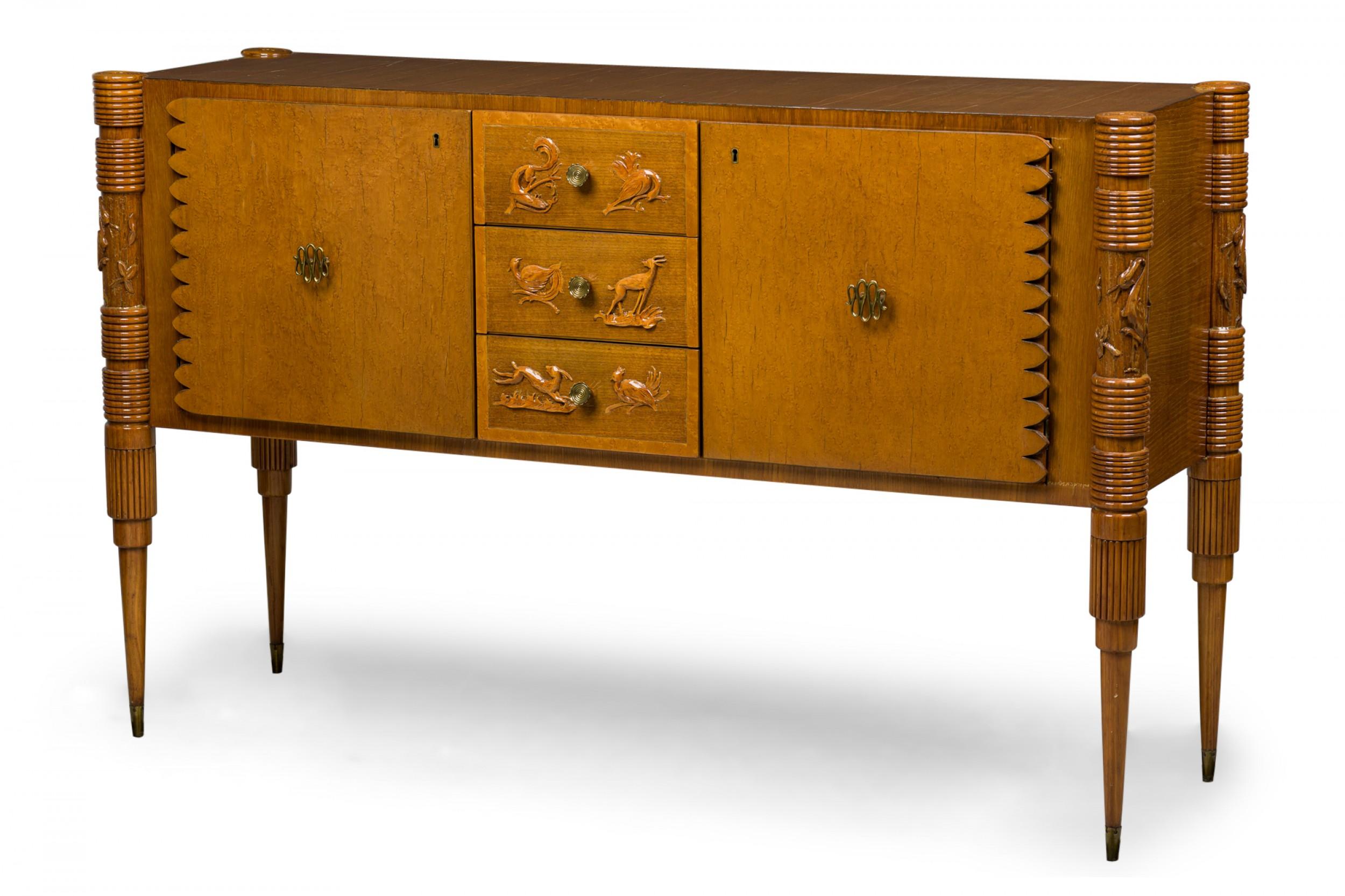 Italian midcentury (1950s) sideboard with a burled birch veneer, having two exterior cabinet doors with ribbon design brass door pulls and a scalloped carved edge, centering three drawers with carved bird decorations on the fronts with small brass