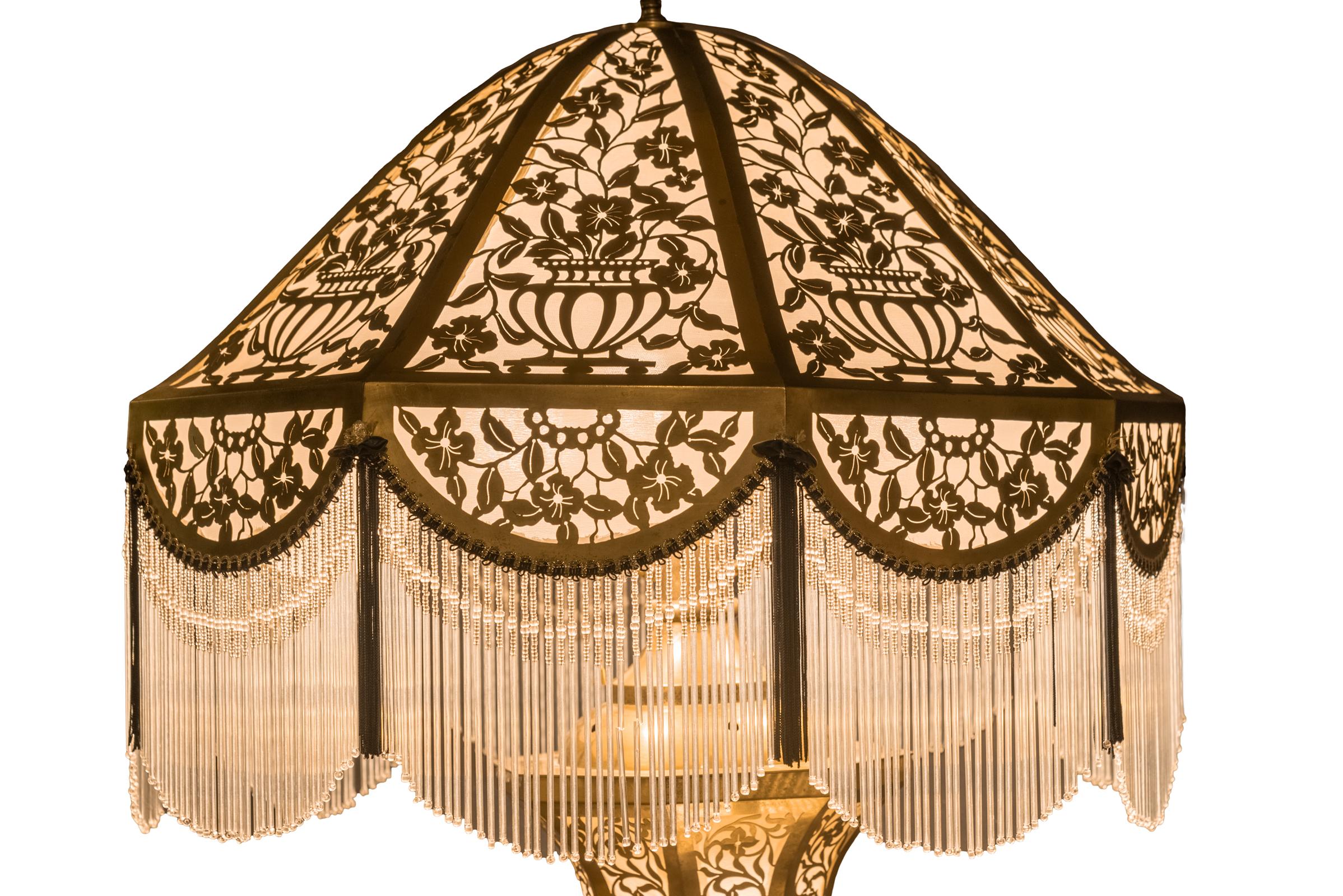 Pierced brass lamp with matching shade and pedestal. A silk-backed pierced brass lamp with matching bead-fringed shade and pedestal. Body of lamp and pedestal are lighted from within, early 20th century, American.

Size: 76 x 25 in. diameter.
