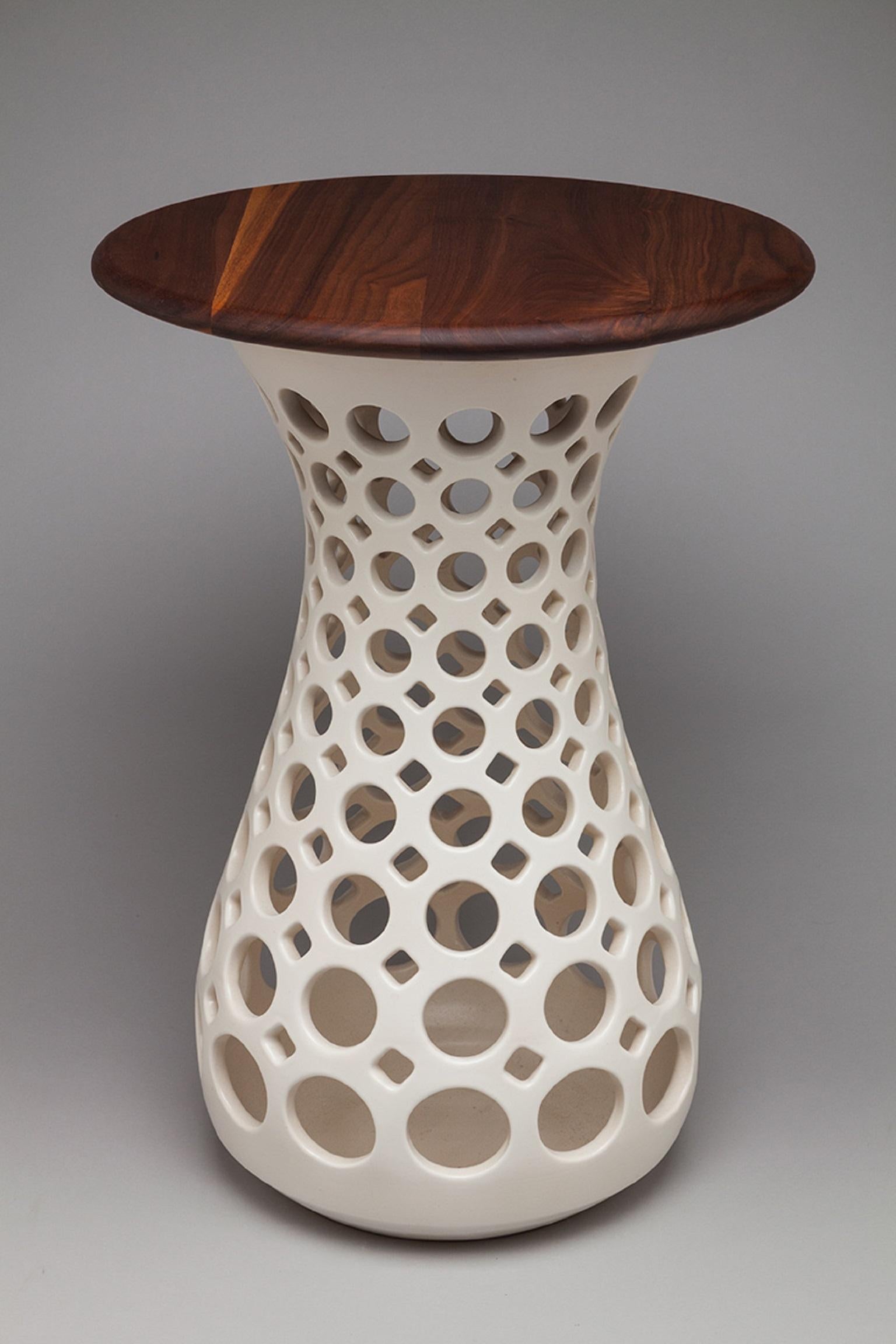 This ceramic side table is thrown on a potter's wheel and then hand pierced. It is fired with a white satin glaze that is luxury to the touch. The finished walnut table top is a separate piece that fits into the base with a lip underneath to help