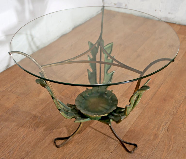 This table has been designed by Pier Luigi Colli with brass feet ending with thin ribbons, and they support the round glass shelf. The brass construction has three large simplified but very decorative leaves that contain a small wooden tray in the