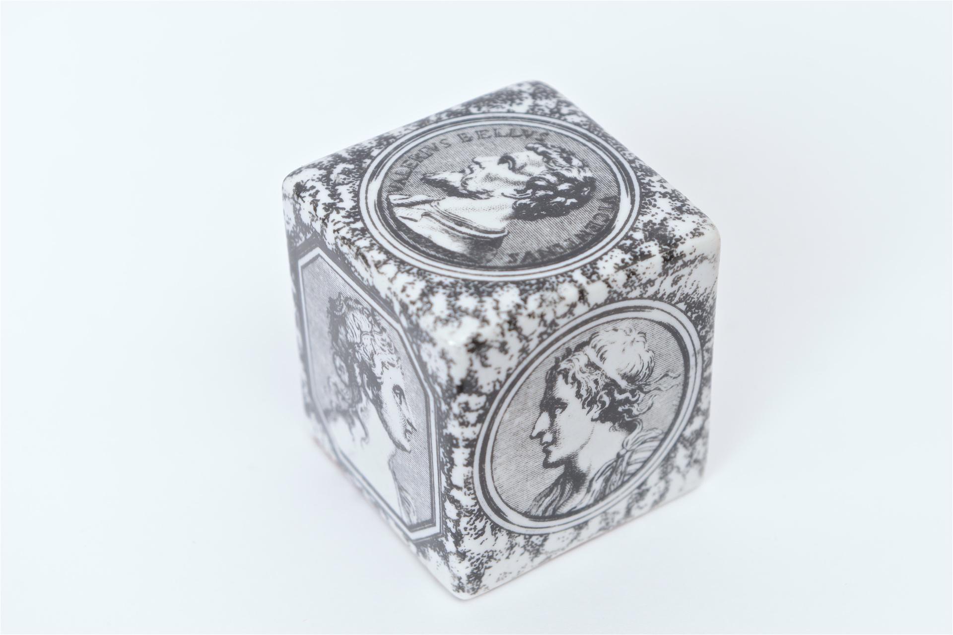 A rare cubic paperweight from the 1950s designed by Piero Fornasetti. This black and white porcelain paperweight is decorated on each side of the cube with the profiles of six Roman heads. Another identical paperweight was seen as part of the family