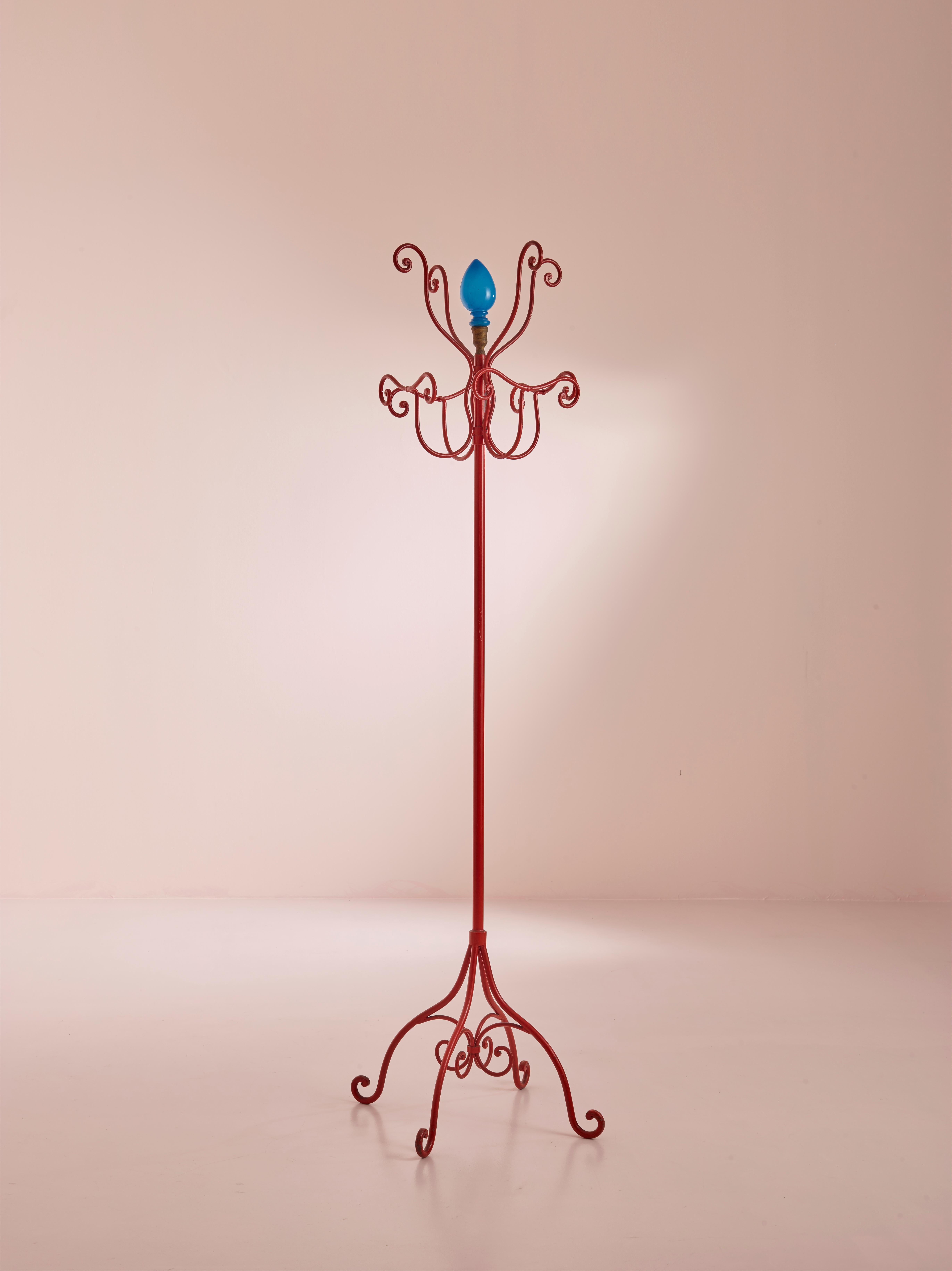 A beautiful coat hanger designed by Piero Fornasetti and produced in the 1960s. 
Made of a wrought iron structure painted in an vibrant red, it can be distinguished by its blue opaline glass on top and high quality construction enriched with brass