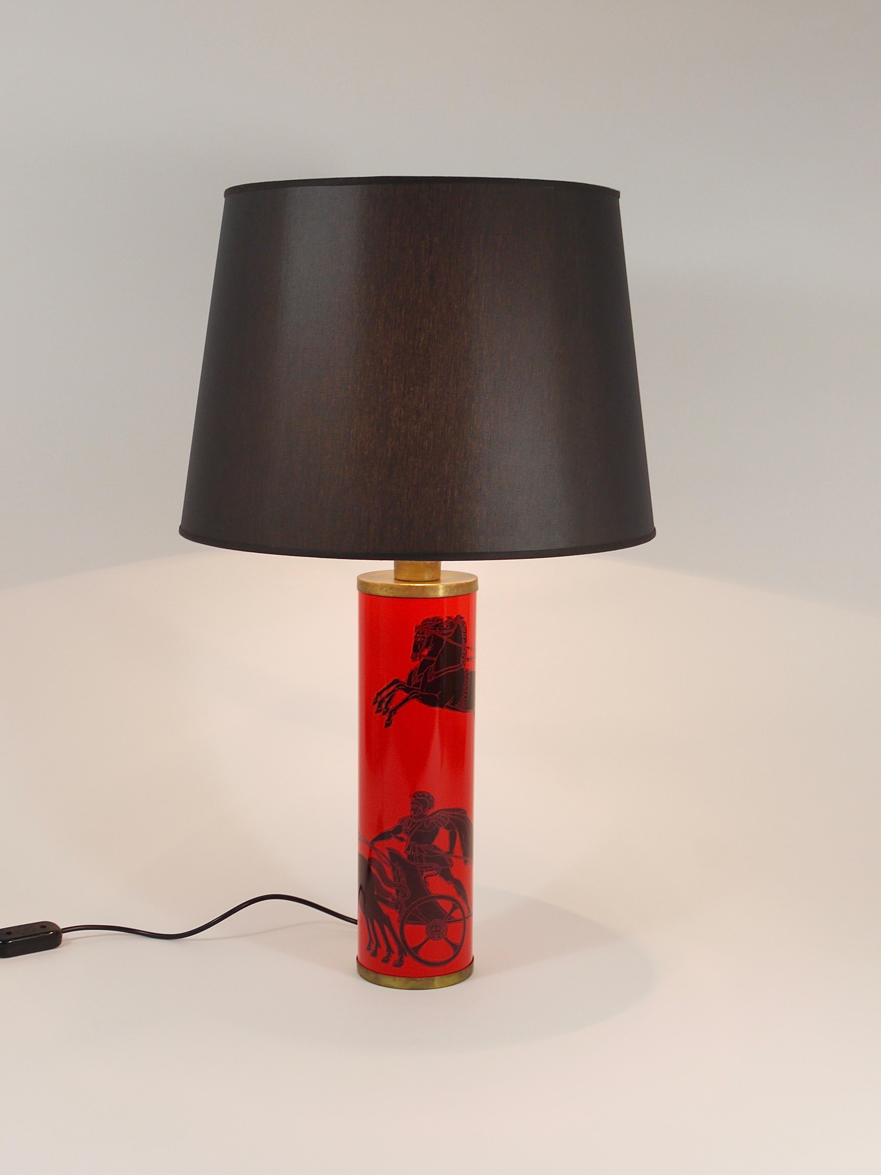 A red and black cylindrical table or side lamp from the 1950s, designed by Piero Fornasetti for Atelier Fornasetti, Milan, Italy. Crafted from metal and brass, the lamp features lithographically transfer-printed warriors on their chariots. This
