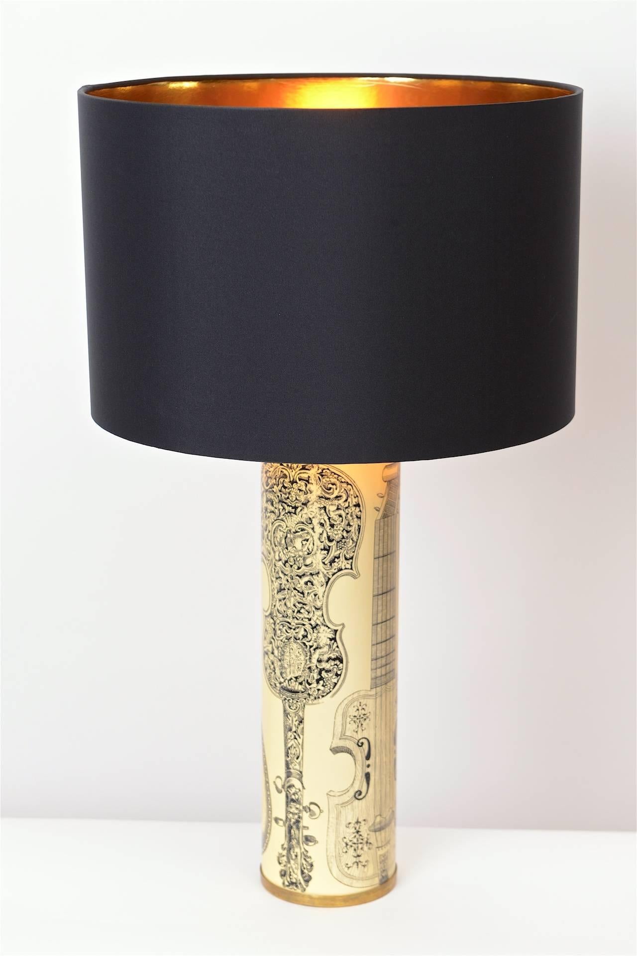 A beautiful, 1950s Italian table lamp by Piero Fornasetti. The cylindrical body of the lamp is decorated with lacquered black transfers of musical instruments on a cream background. The lamp comes complete with a new shade and has been newly