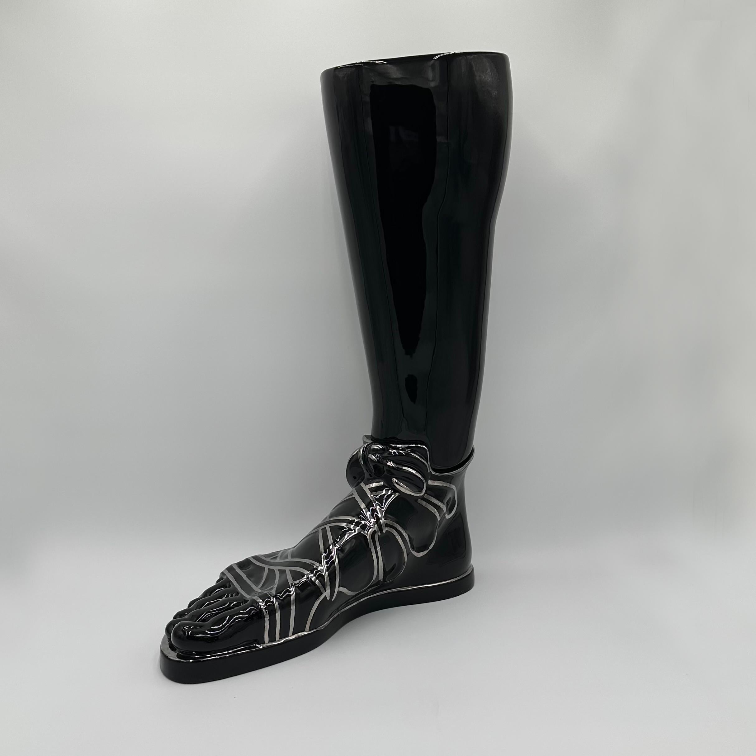 The Piero Fornasetti Stick or Umbrella Stand consists of a hollow glazed ceramic black leg and detailed foot, dressed in a Greco-Roman style sandal. The sandal is hand-painted in silver. This piece is rare and very collectible. 

Piero Fornasetti,