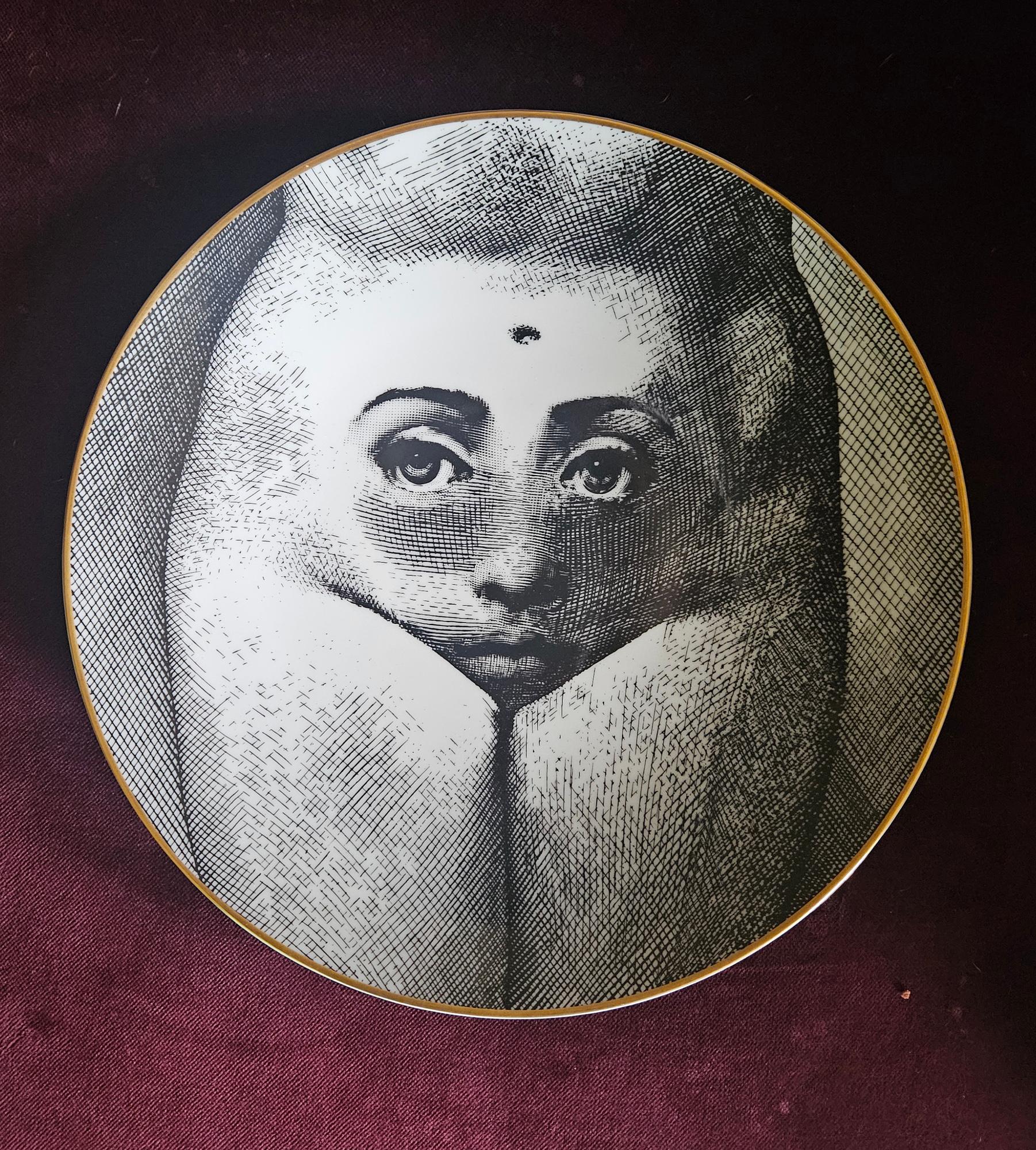 Piero Fornasetti Assiette en porcelaine Rosenthal Thèmes et variations, 
Motivation numéro 19,
Le Baubo,
Avec la boîte noire d'origine,
1980s

La plaque imprimée en noir et blanc, bordée d'or, représente un corps de femme nue avec, sur le ventre, le