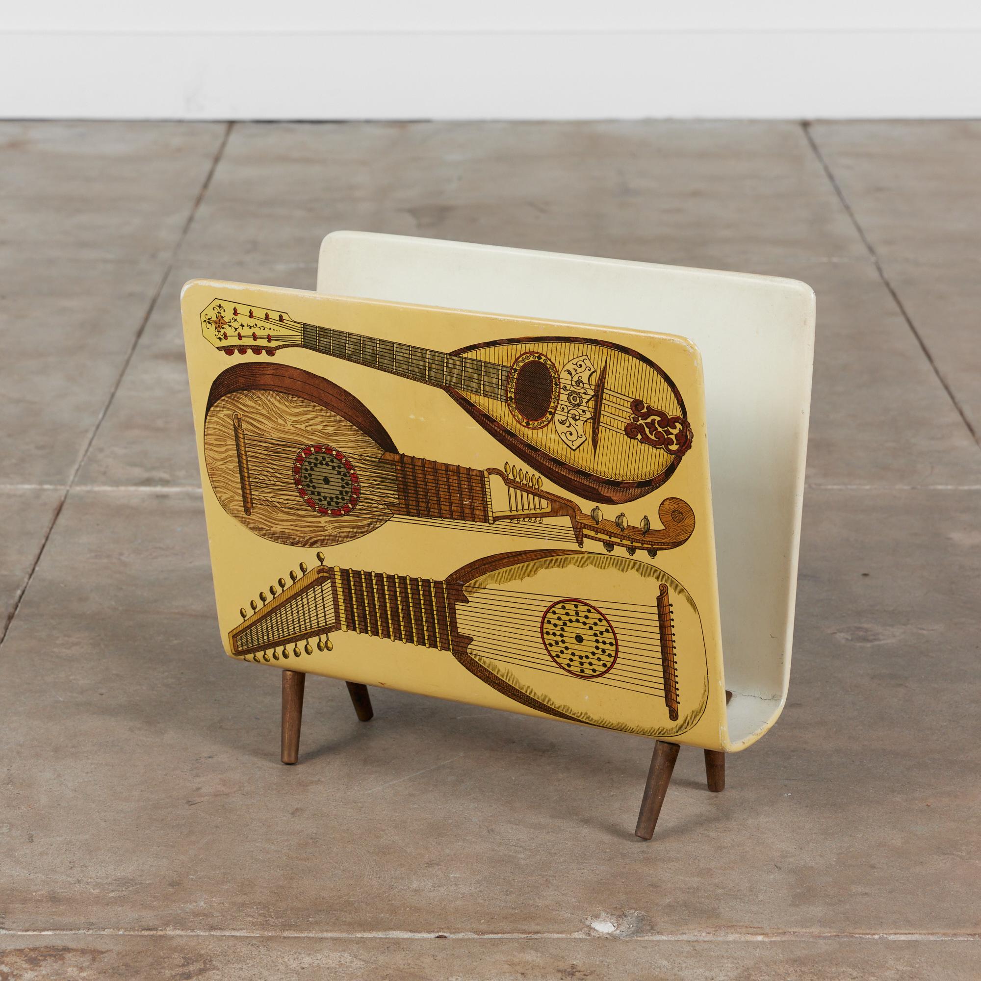 Magazine rack by Italian designer and artist, Piero Fornasetti, circa 1950s, Italy. The rack features a musical themed lithograph printed on plywood with a wire brass divider on the interior with four splayed brass feet.

Dimensions
16.75
