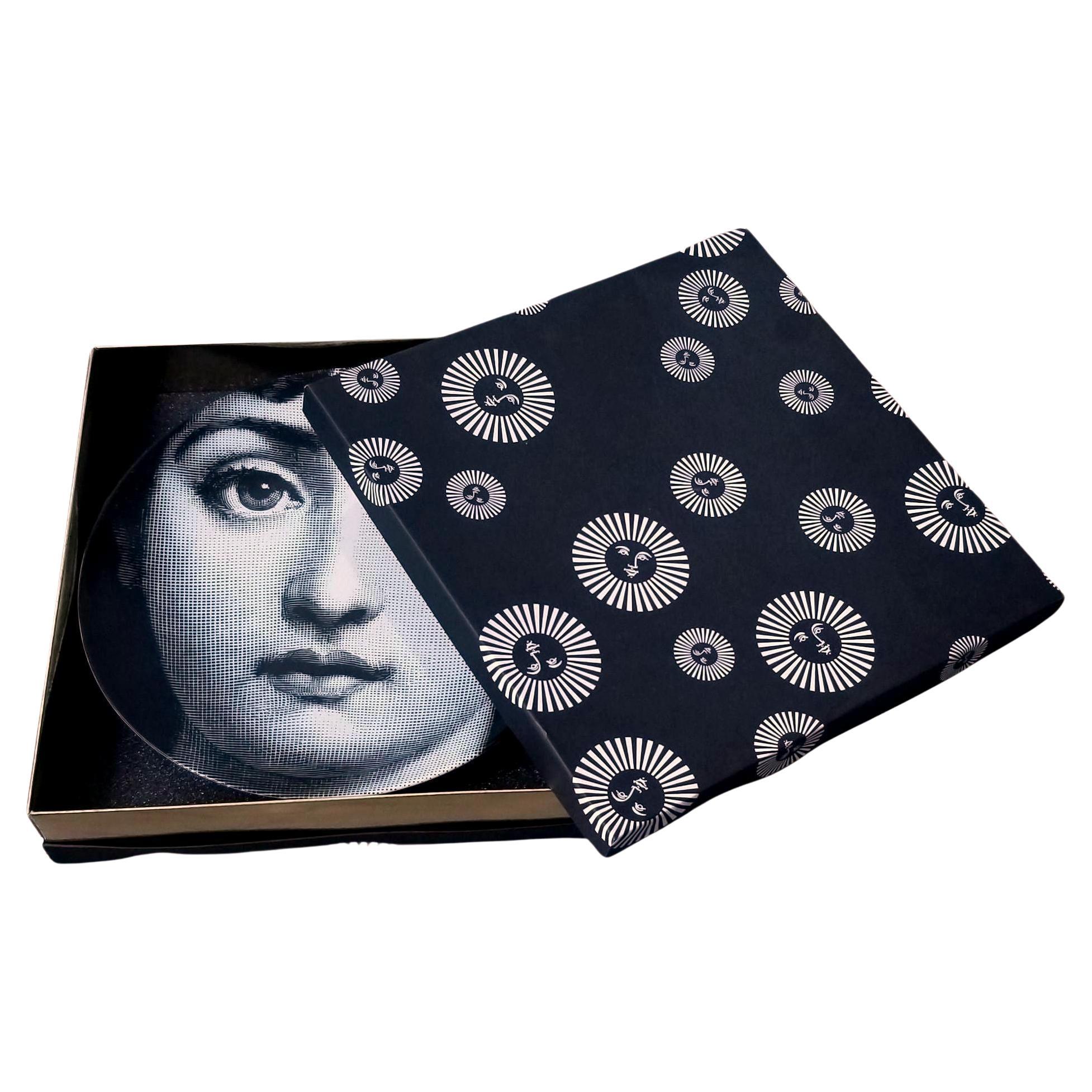 Il volto della cantante lirica Lina Cavalieri, musa di Piero Fornasetti, impreziosisce questo piatto decorativo da parete in porcellana. Questa è la prima decorazione di quella che è diventata l'iconica serie Tema e Variazioni. Questo piatto in