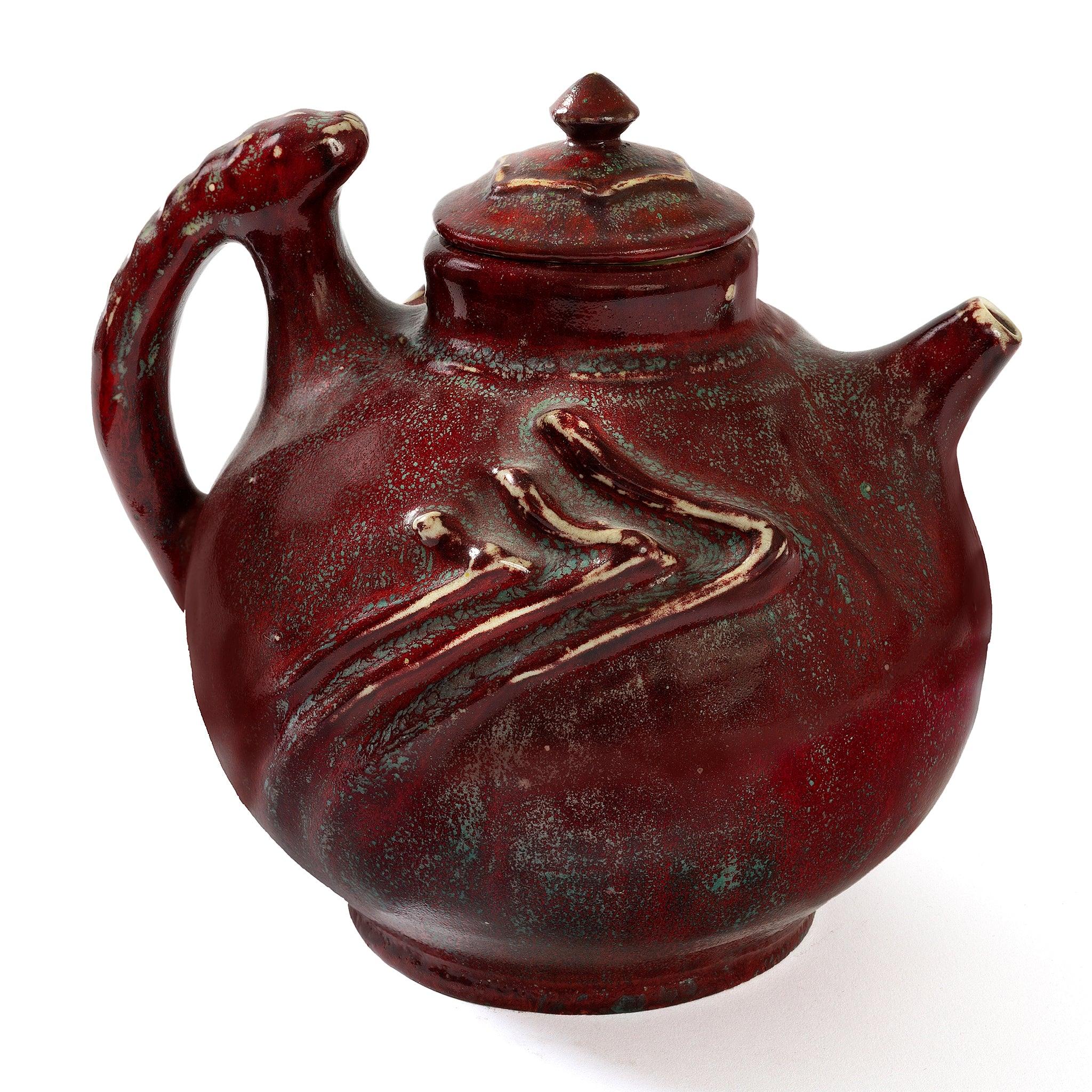 A ceramic lidded teapot by Pierre-Adrien Dalpayrat featuring a spherical body decorated with dynamic sculptural ribs, an inventive crescent-shaped handle, a saucy spout, and a particularly rich burgundy example of Dalpayrat’s signature glaze. Relief