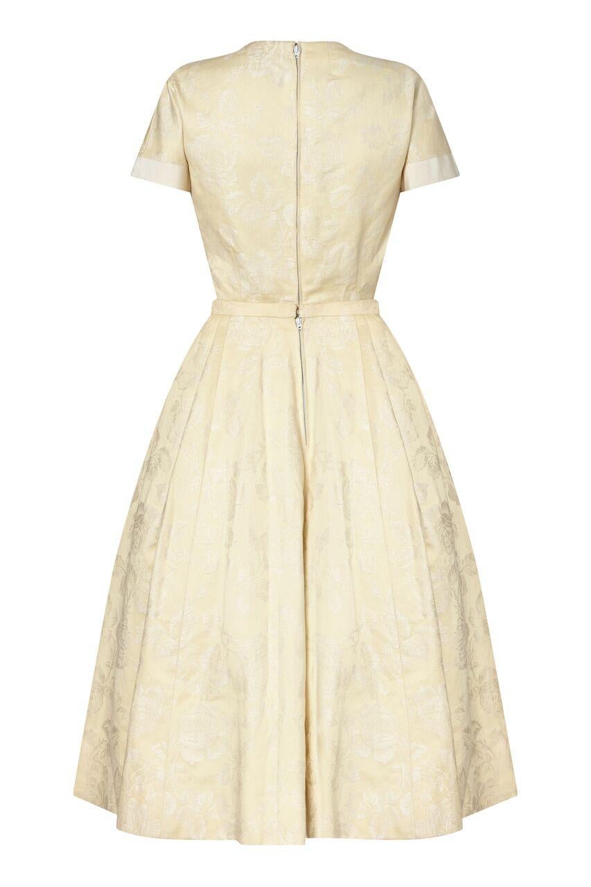 This timeless 1950s New Look style Haute Couture two piece by Pierre Balmain is in impeccable condition with exceptional line and form. The soft cream jacquard fabric is embossed with a romantic rose design and features wide bands of ivory grosgrain