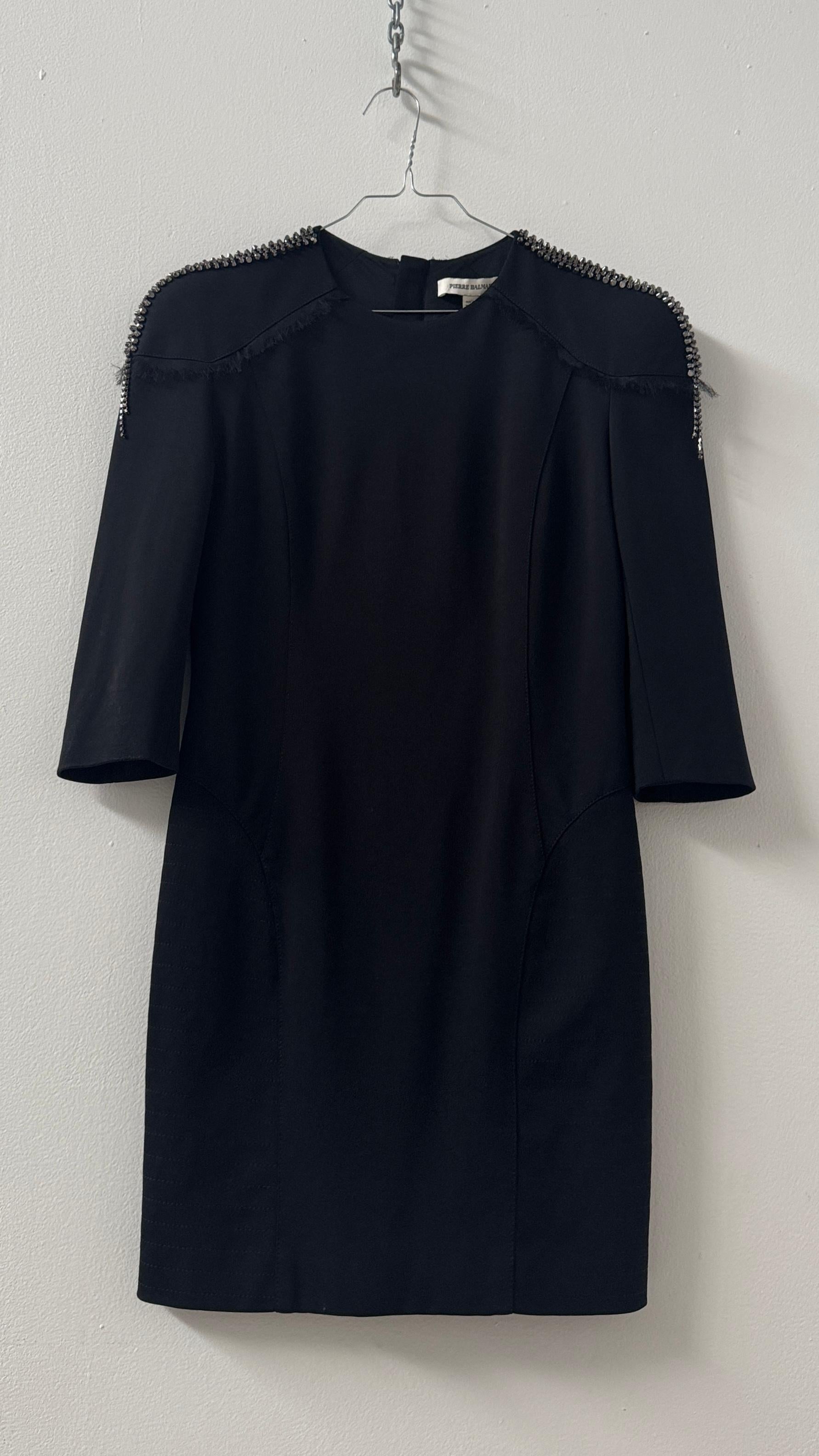 Ein elegantes Statement mit einem kühnen Twist: Dieses schwarze Kleid von Pierre Balmain fängt die raffinierte und doch kantige Ästhetik der Marke perfekt ein. Es ist aus einem strukturierten Stoff gefertigt, der die Silhouette betont, und zeichnet