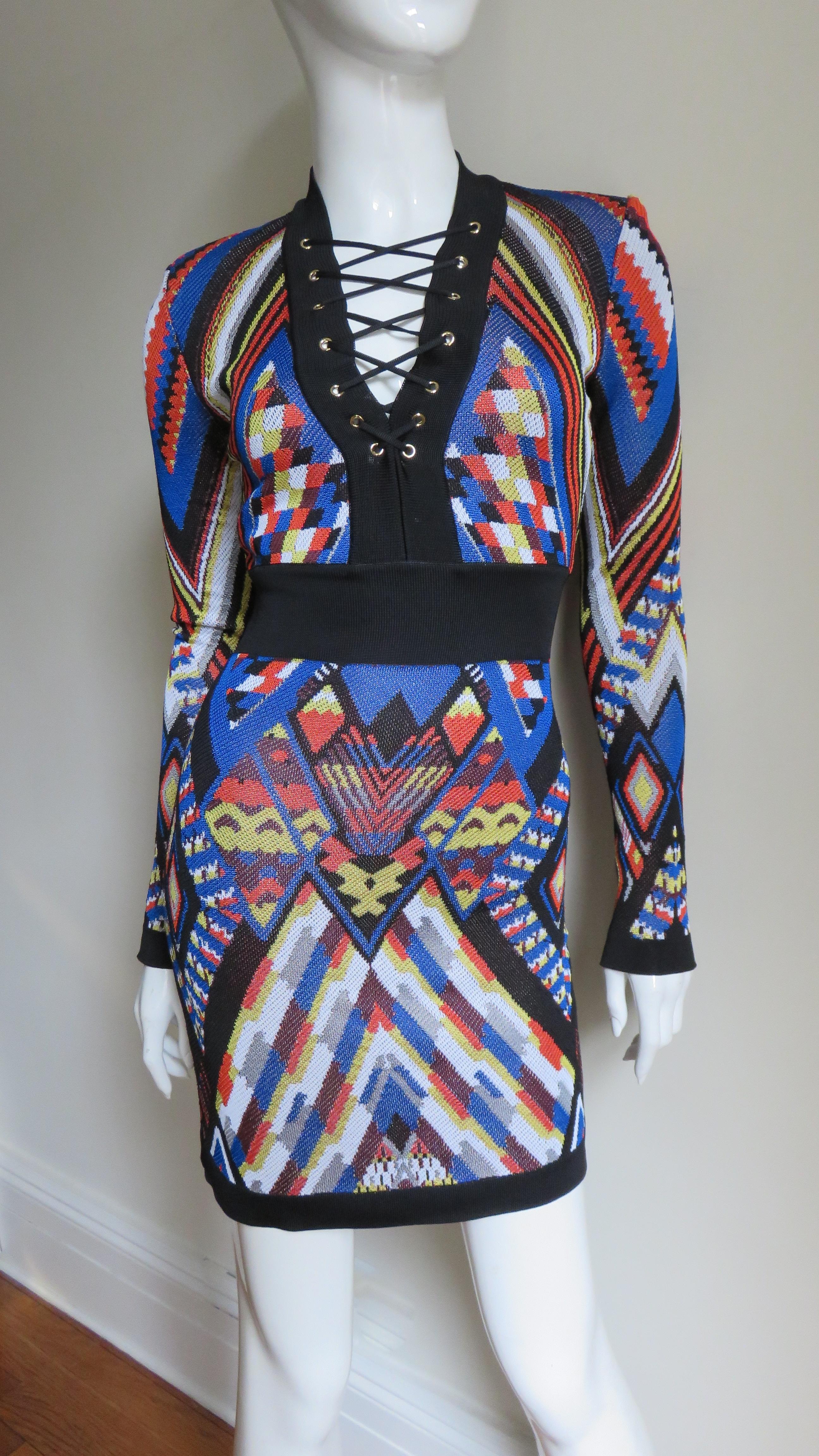 A gorgeous geometric ikat print stretch dress from Pierre Balmain in red, blue, yellow, black and white.  It has long sleeves and a V neckline with functional black lacing to just below the bust.  The trim on the neckline, cuffs, hem and band at the