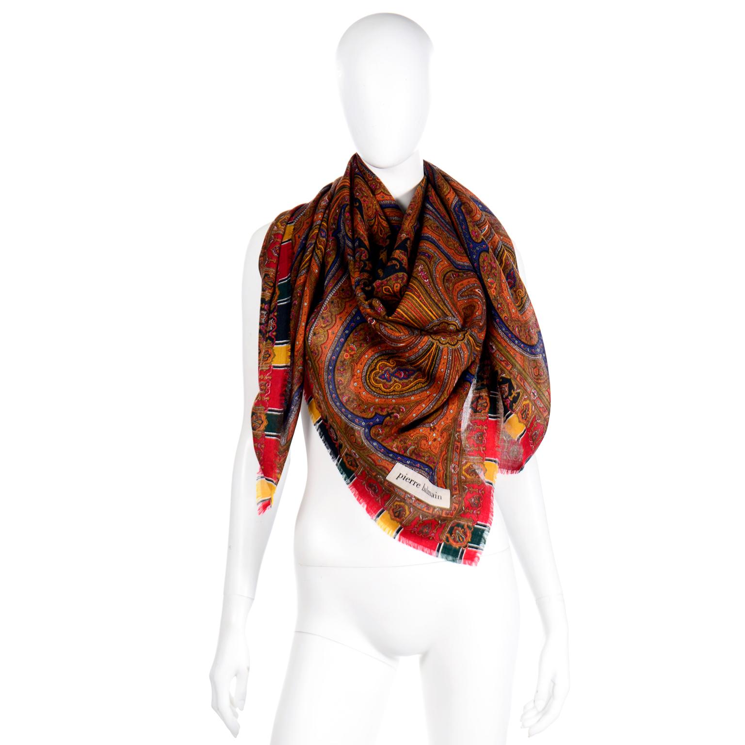 This is a gorgeous oversized vintage paisley Pierre Balmain wool scarf in vibrant fall colors that include red, green, pumpkin orange, marigold, dark blue, red, gold, black, and white. Made of 100% fine wool with pretty fringed edges. The corner of