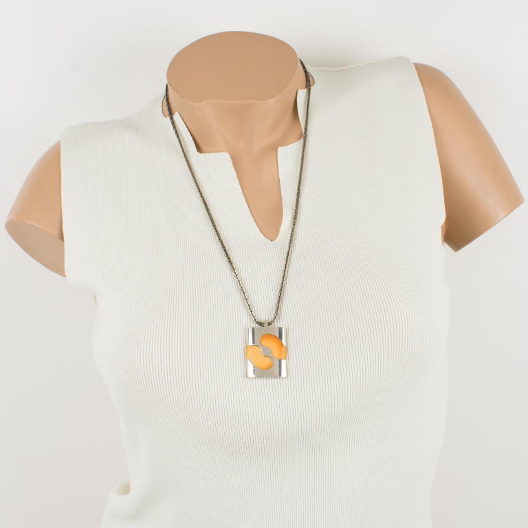 Lovely Pierre Cardin modernist 1970s necklace. Extra-long silverplate metal worked chain with Mod pendant. The pendant features a geometric design with a silvered metal framing ornate with orange resin inserts. Box closing clasp with Cardin logo. It