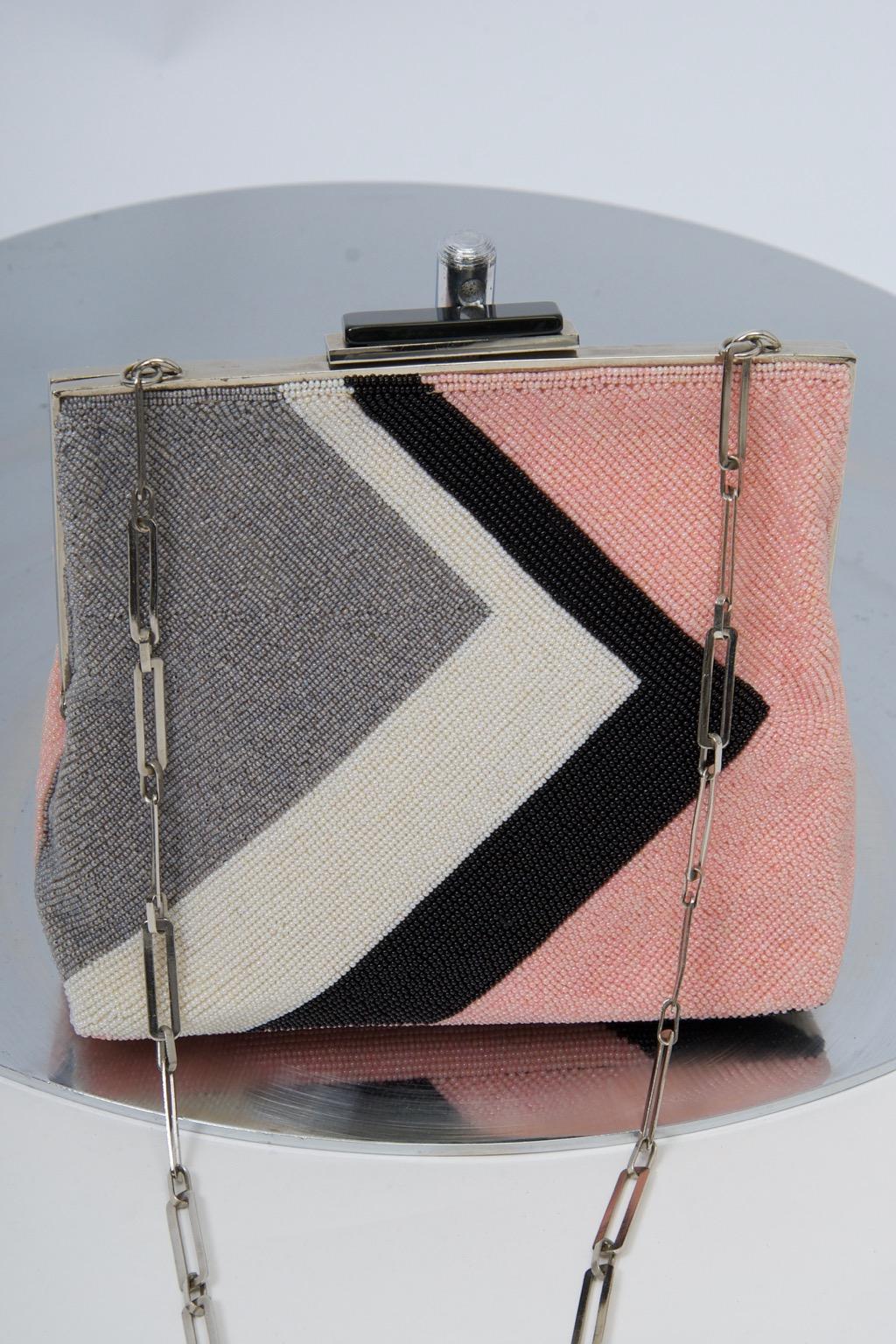 Pierre Cardin produced a line of beaded bags duirng his prime years that featured his favored geometric motifs and are highly collectible. This example, crafted of pink, gray, white and black micro beads, highlights a sideways V orientation, with