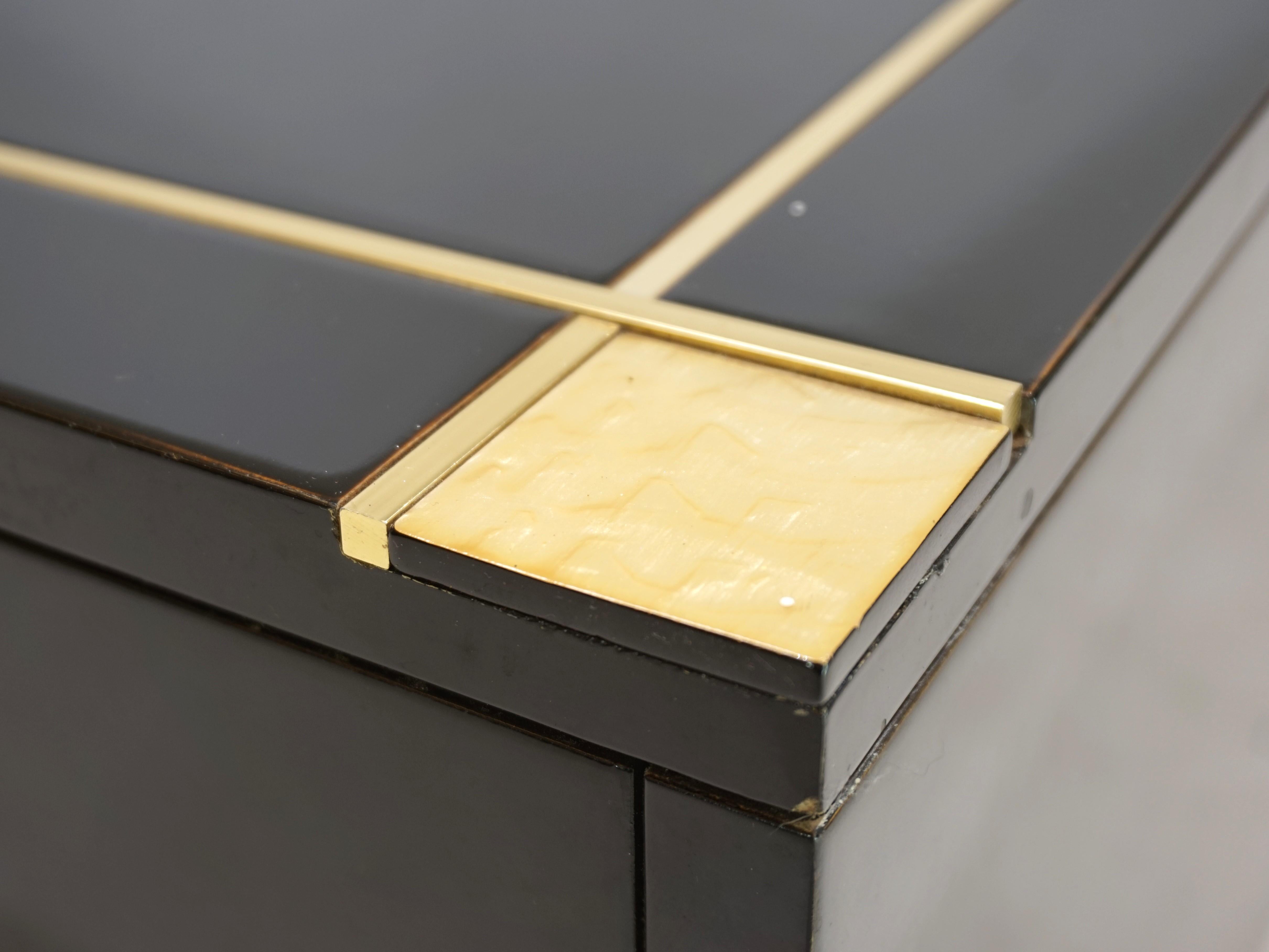 Une table basse exclusive de Pierre Cardin en laque piano noire. La table comporte des tiges de laiton éblouissantes, qui sont incorporées dans deux côtés et dans le plateau de la table. Les coins de la table sont ornés de coquillages dorés et