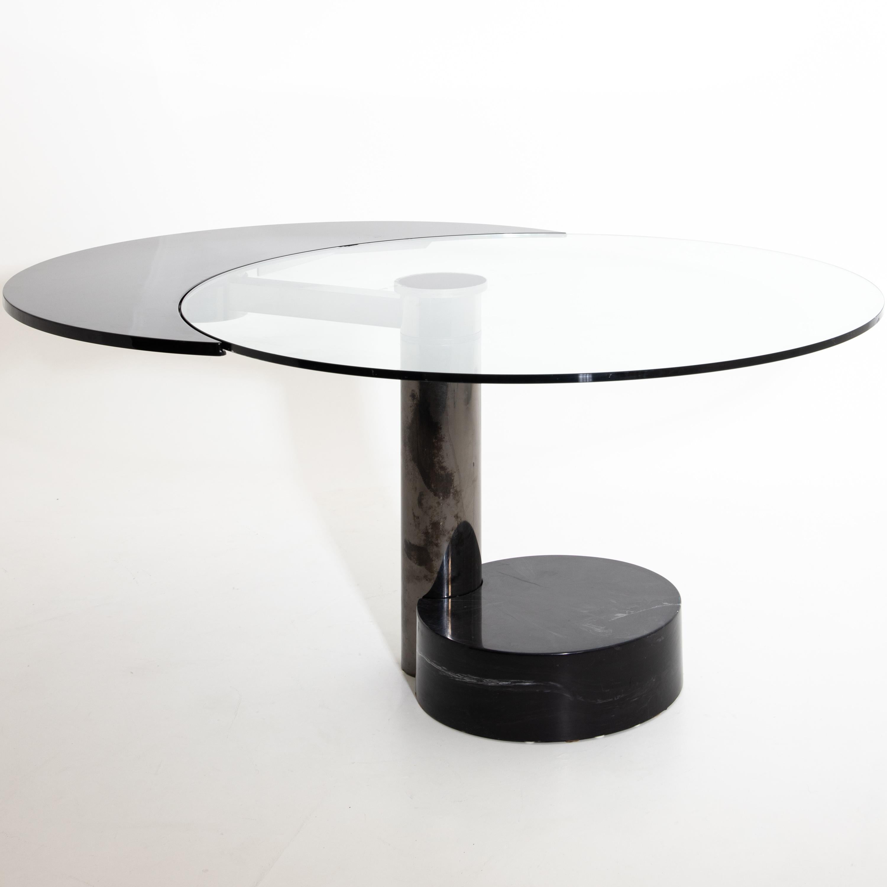 Round dining table by Pierre Cardin with revolving tabletop in black as an extendable element that changes the tabletop’s shape from round to oval. The table stands on a cylindrical stainless-steel base with a black round artificial stone base.
 