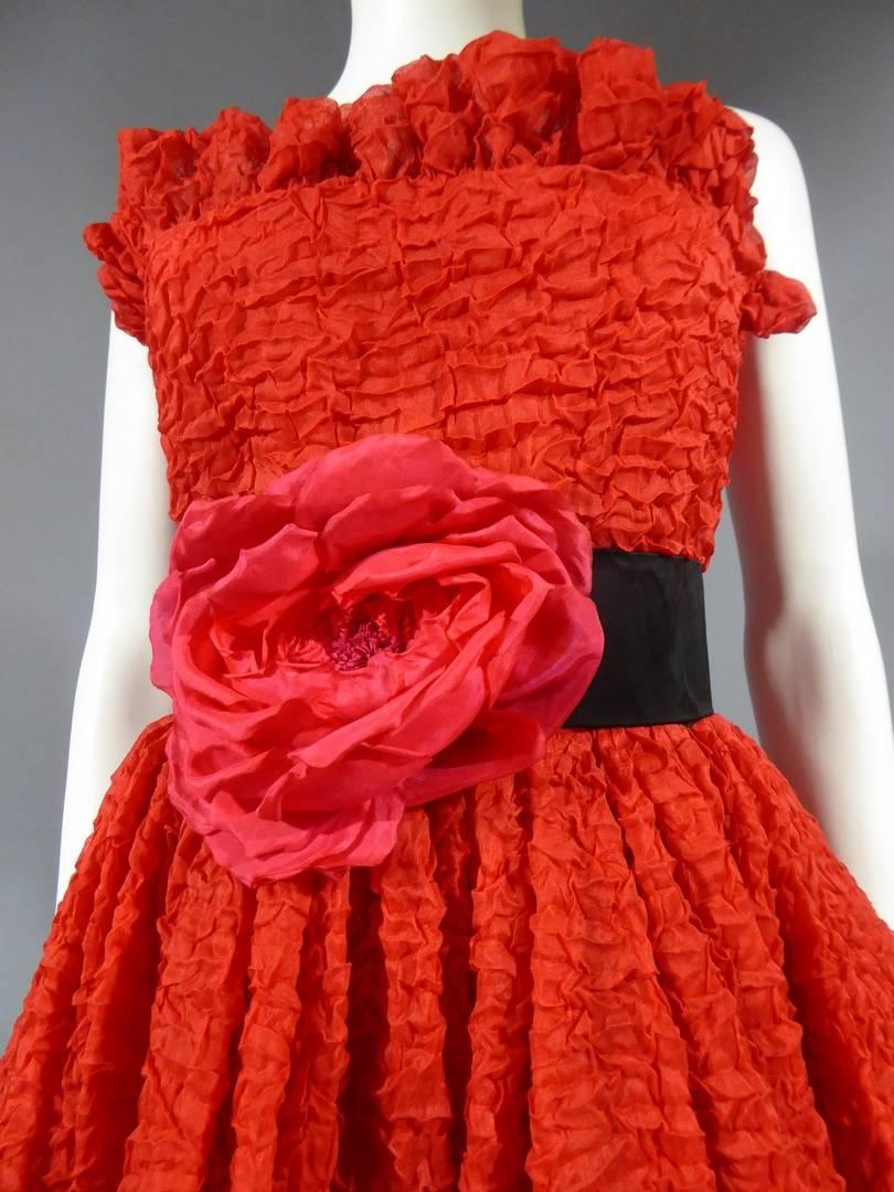 Circa 1980

France

Pierre Cardin Haute Couture strapless cocktail dress in red bubbled silk. Skirt of the short dress on the front of the long dress on the back. Borders of the skirt and bustier in the same and flying. Marked size. Red silk lining.
