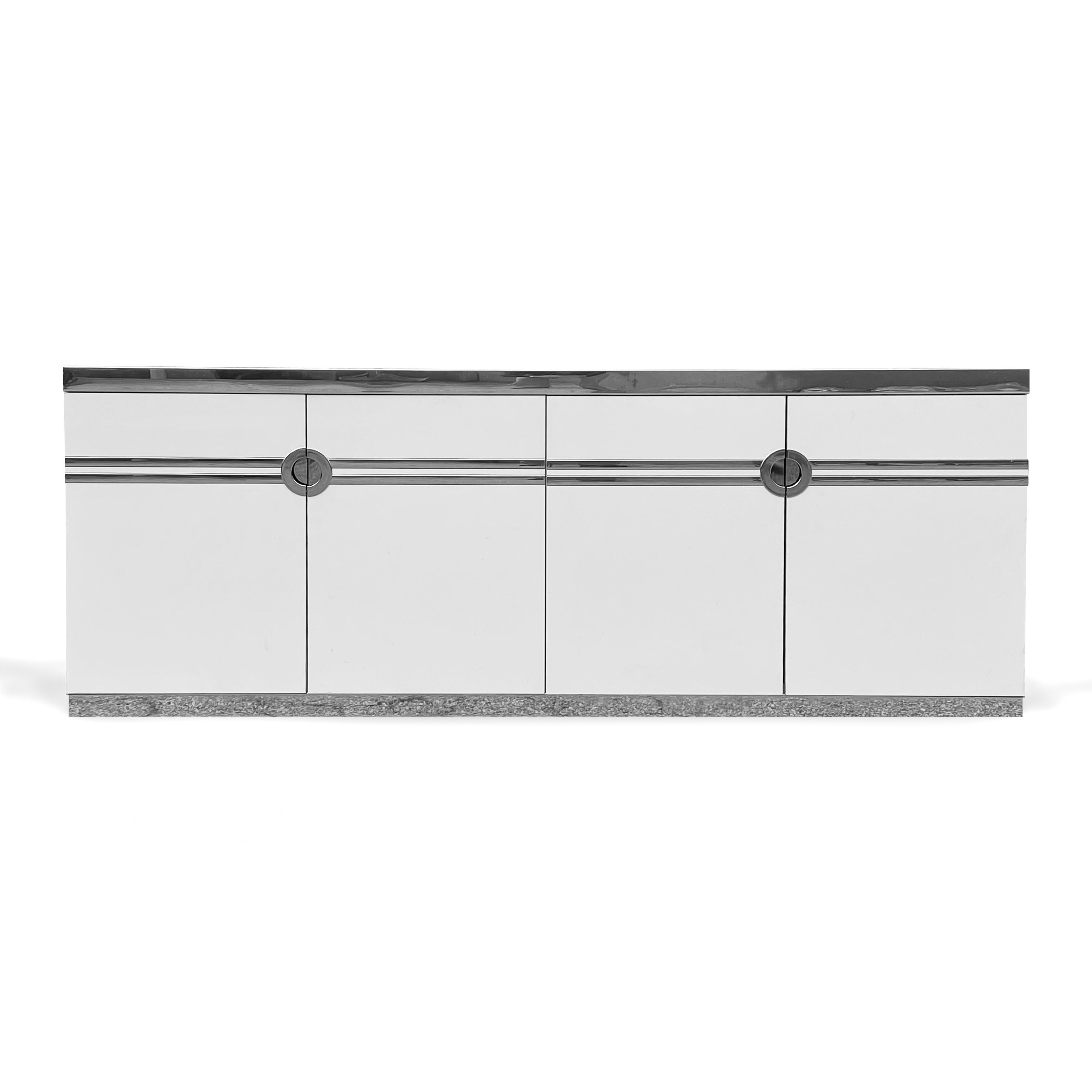 A sleek and sophisticated 1970s design by Pierre Cardin, this long, low white cabinet has linear graphic elements and recessed pulls in chrome. The piece references art deco design, but is decidedly modern. Four doors conceal two cabinets each with