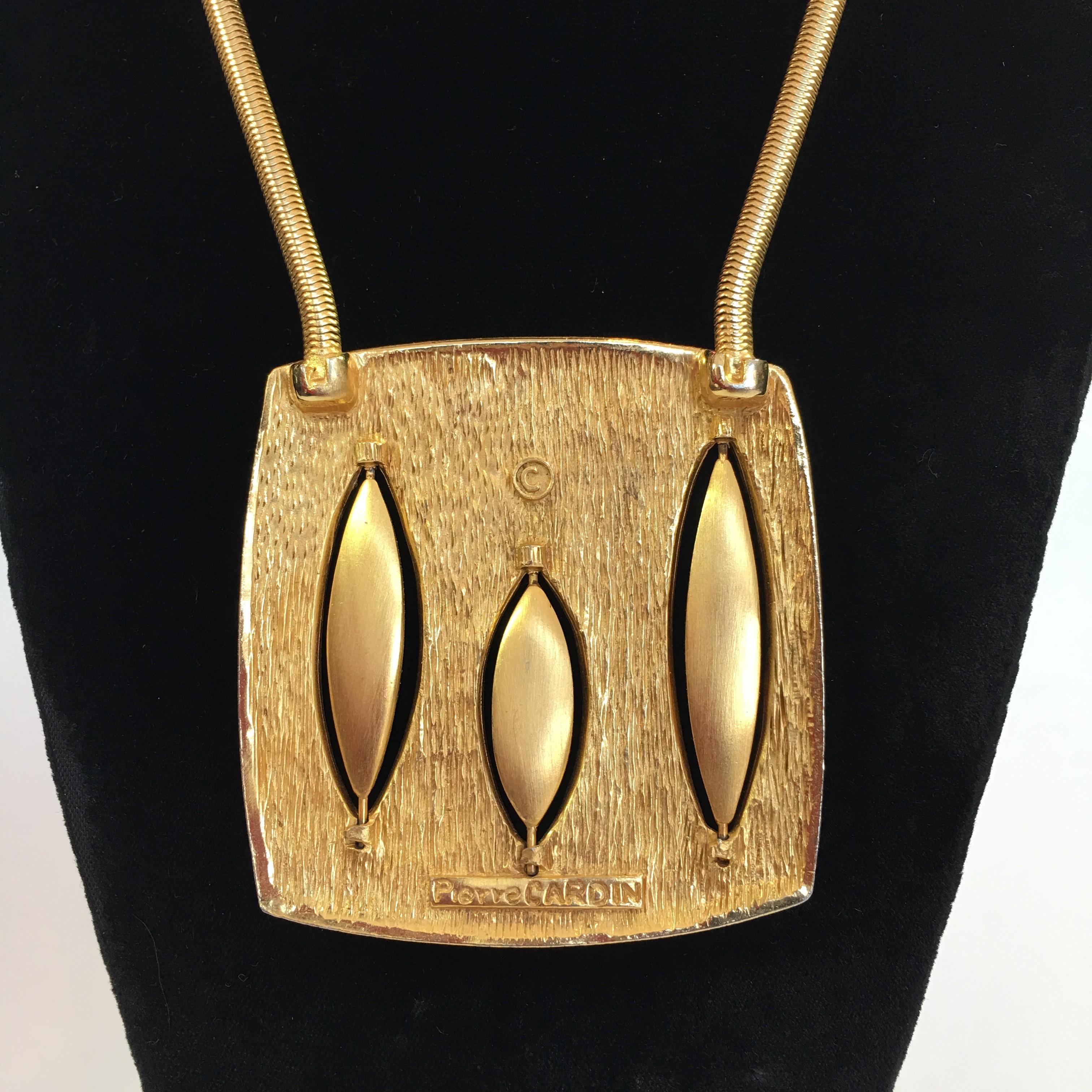 Pierre Cardin Mid-Century Modern Gold Tone + Enamel Necklace from the 1960's. Flat snake chain connected to each side of the pendant. Custom Cardin clasp at back of neck. 
Necklace is in very good vintage condition.

Measurements are as