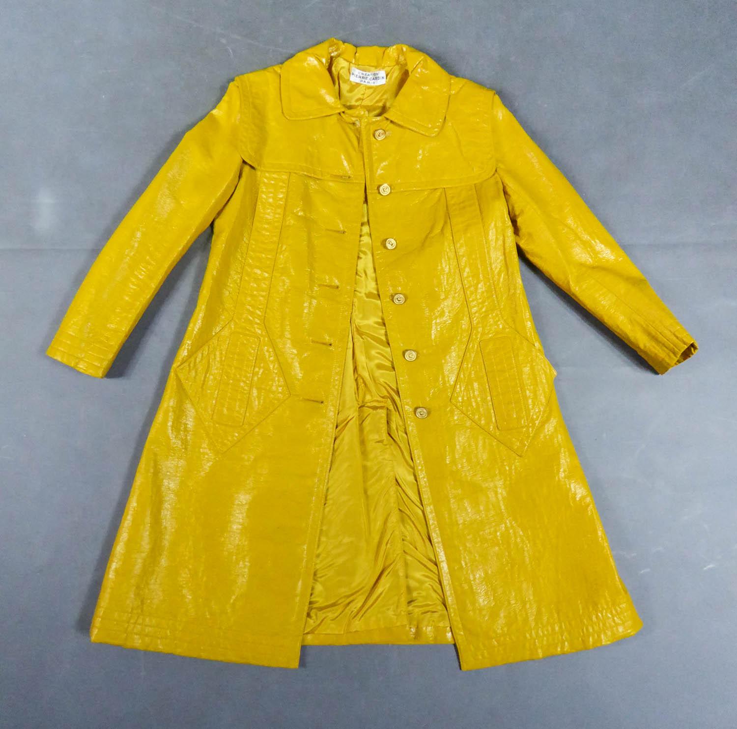 Circa 1970
France

Raincoat in mustard yellow vinyl leatherette by Pierre Cardin from the most modernist period of the famous designer in the early 1970s. Large stitching and appliqué of pocket with geometric diamond pattern on the front. Small
