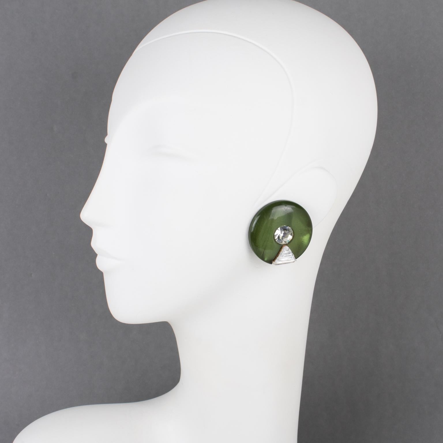 These lovely Pierre Cardin Space Age clip-on earrings were designed in the 1970s. 
The earrings feature a rounded domed shape in pearlized army green Lucite. The earrings have embellishments with clear crystal rhinestones. They are marked at the