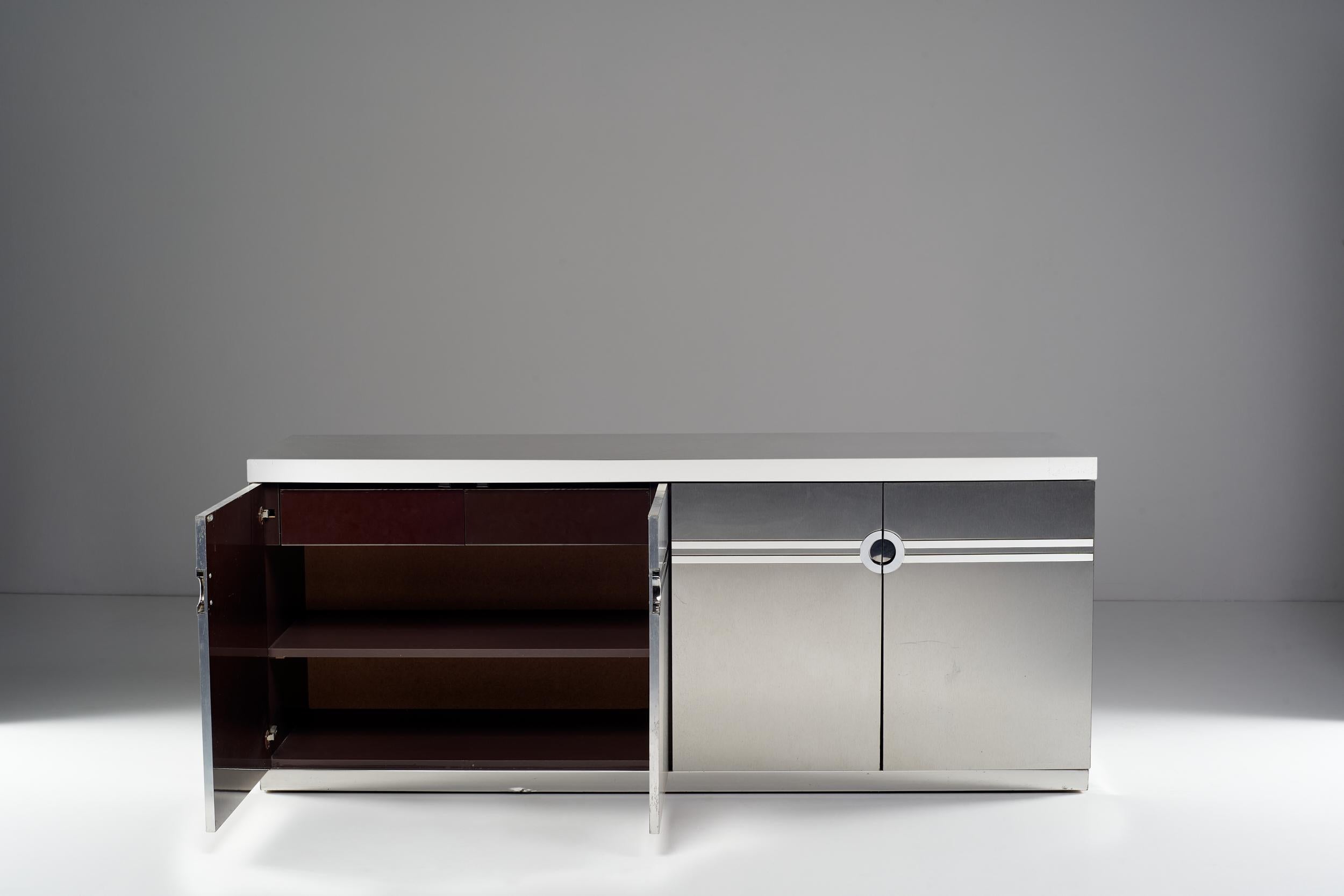 The Cardin sideboard, was designed with a wooden structure and covered with steel and laminate. The decoration of the front plays on the alternation between raw and laminate. The horizontal bands converge in cross-shaped squares and form a 