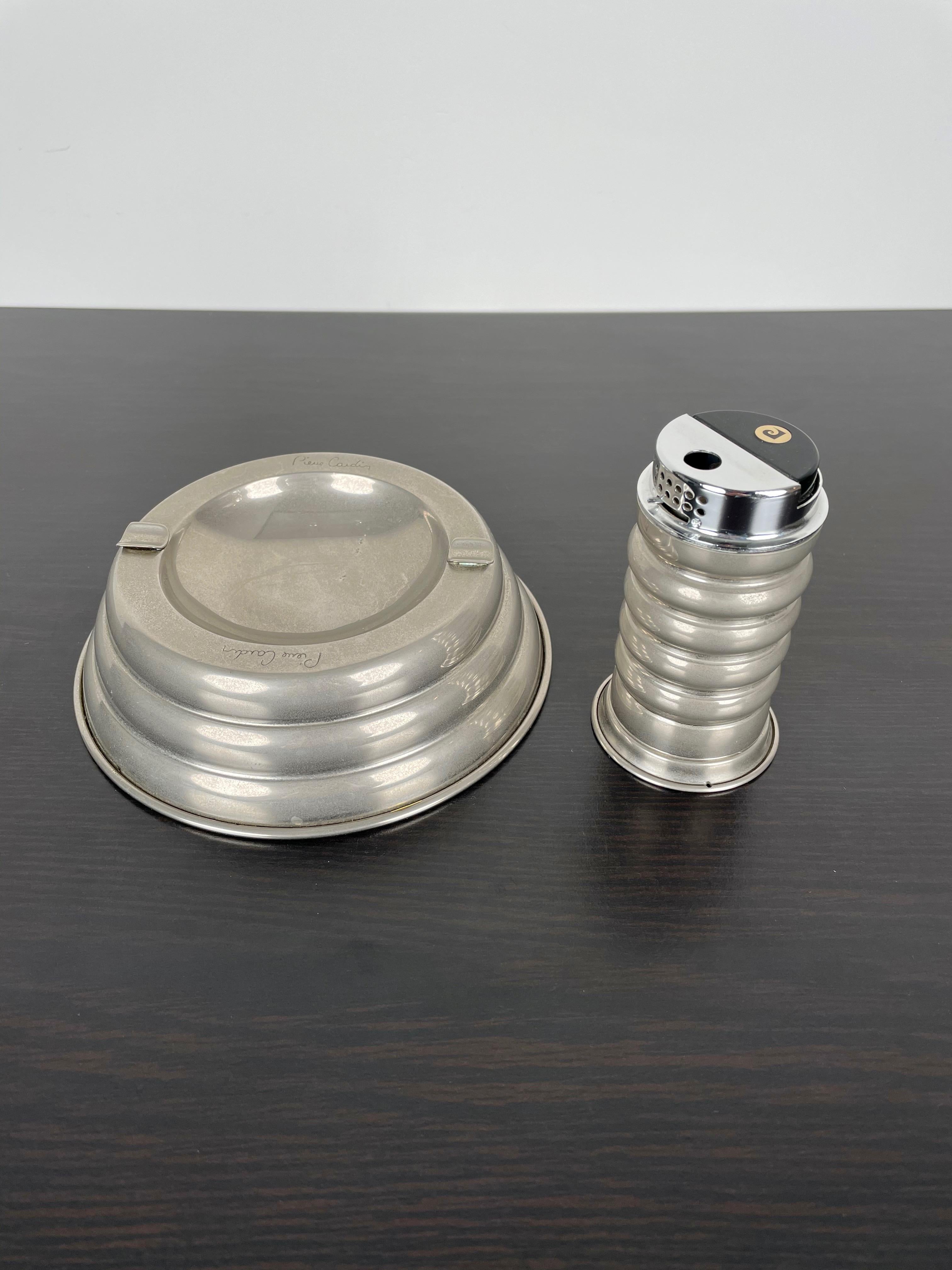 Tobacco table set in metal composed of a lighter and an ashtray made by the French designer Pierre Cardin, Paris, 1970s. 
On both items the designer's signature is engraved and visible, as shown in photos. 

Dimensions:
- Ashtray: Diameter 15 cm