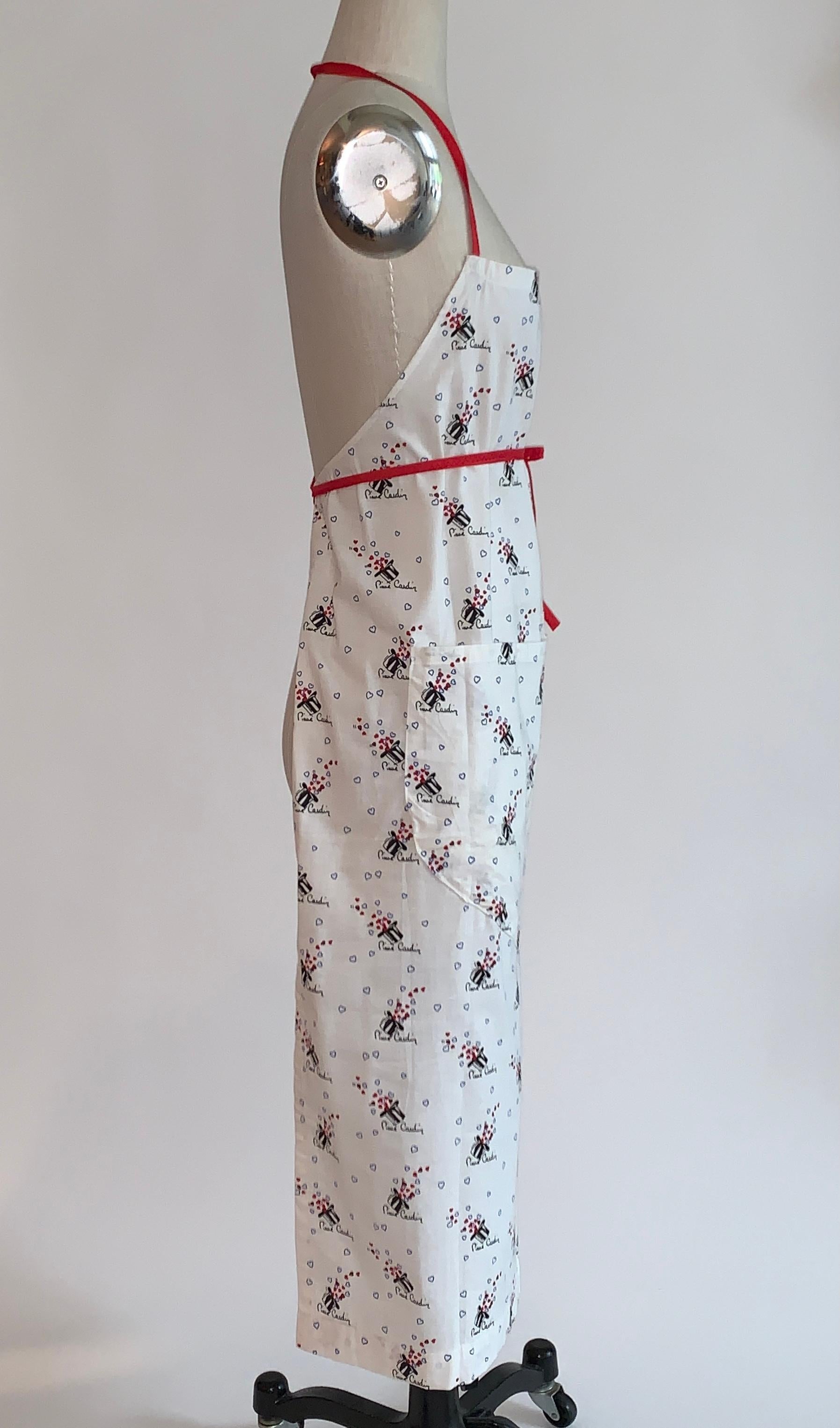 Sehr lustige Vintage-Schürze aus Pierre Cardin Stoff mit schwarzen Zylinderhüten  mit roten und blauen Herzen und der Signatur von Pierre Cardin. Träger im Neckholder-Stil am Oberteil, Bänder in der Taille. 

Die Schürze scheint handgefertigt zu