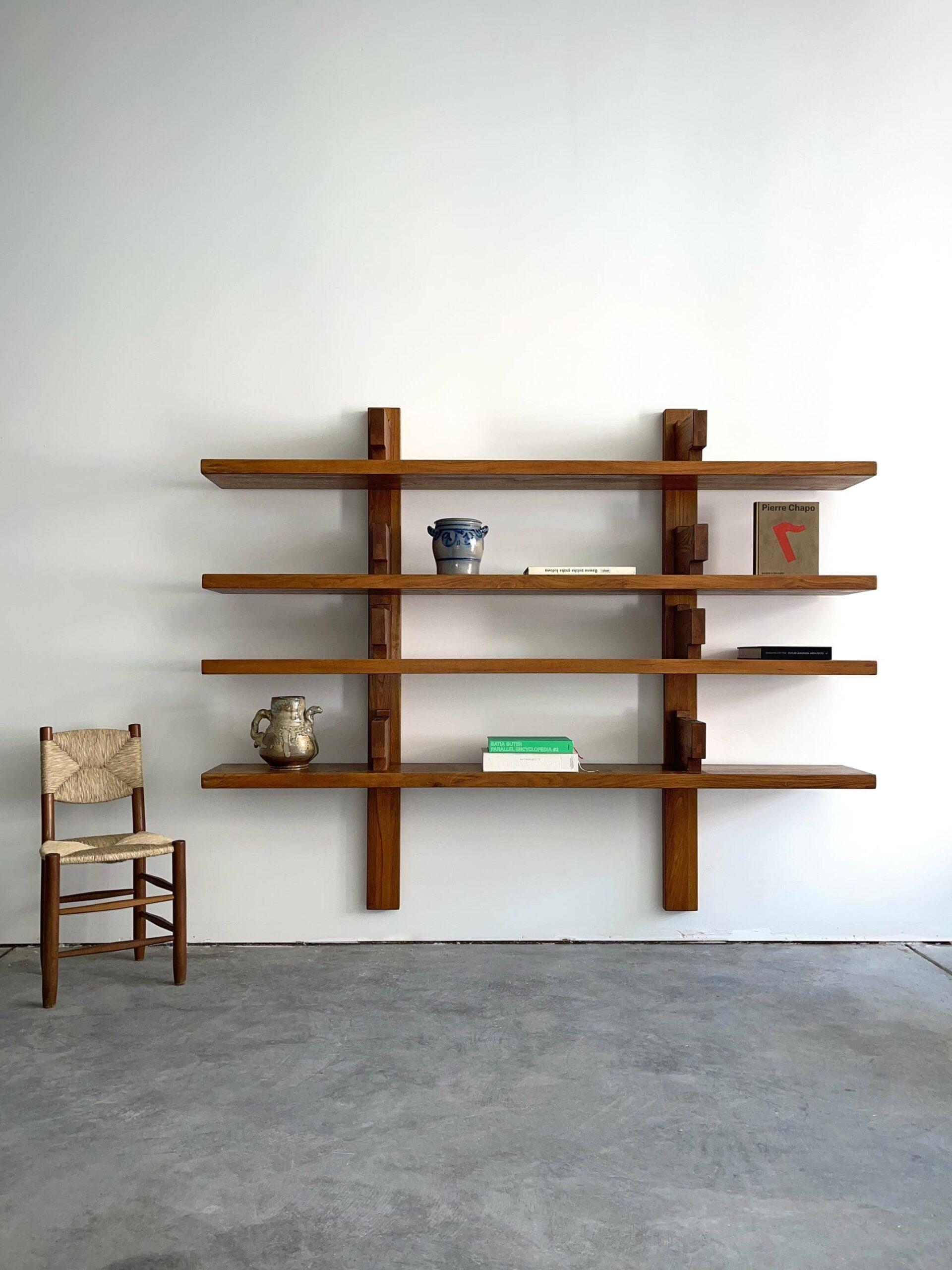 An instantly recognizable Pierre Chapo wall hanging bookshelf consists of 4 horizontal solid elm slats that rests under 8 brackets. Chapo playfully turned this around and put the brackets on top, fixing the construction with elm wedges. This way the