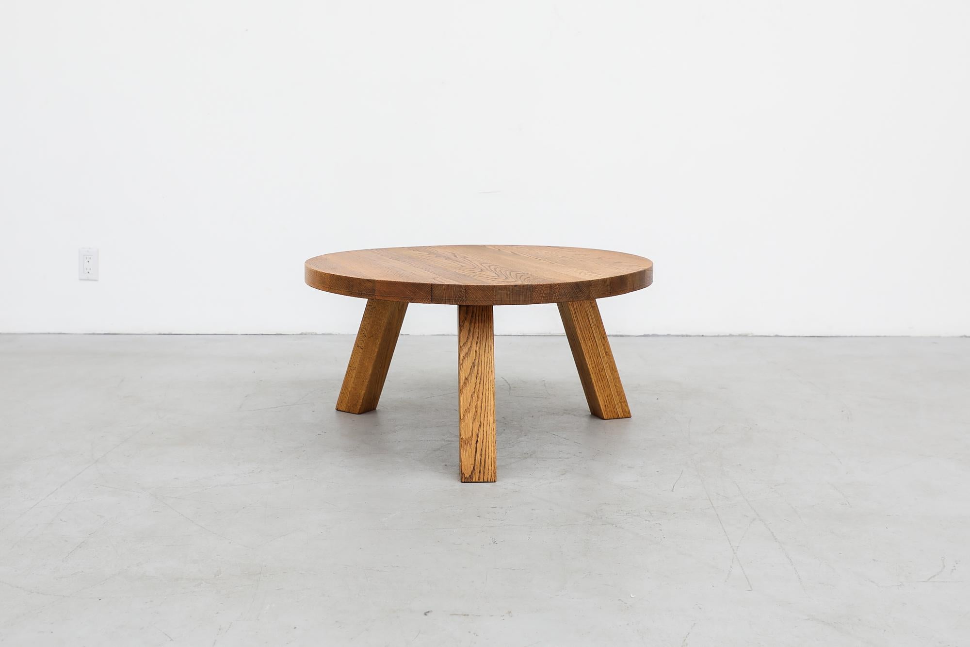This 1970s, Brutalist, heavy, round coffee table is made from solid oak and has three sturdy square tripod legs. The piece is lightly refinished. In otherwise original condition with visible wear and patina consistent with its age and use. Other