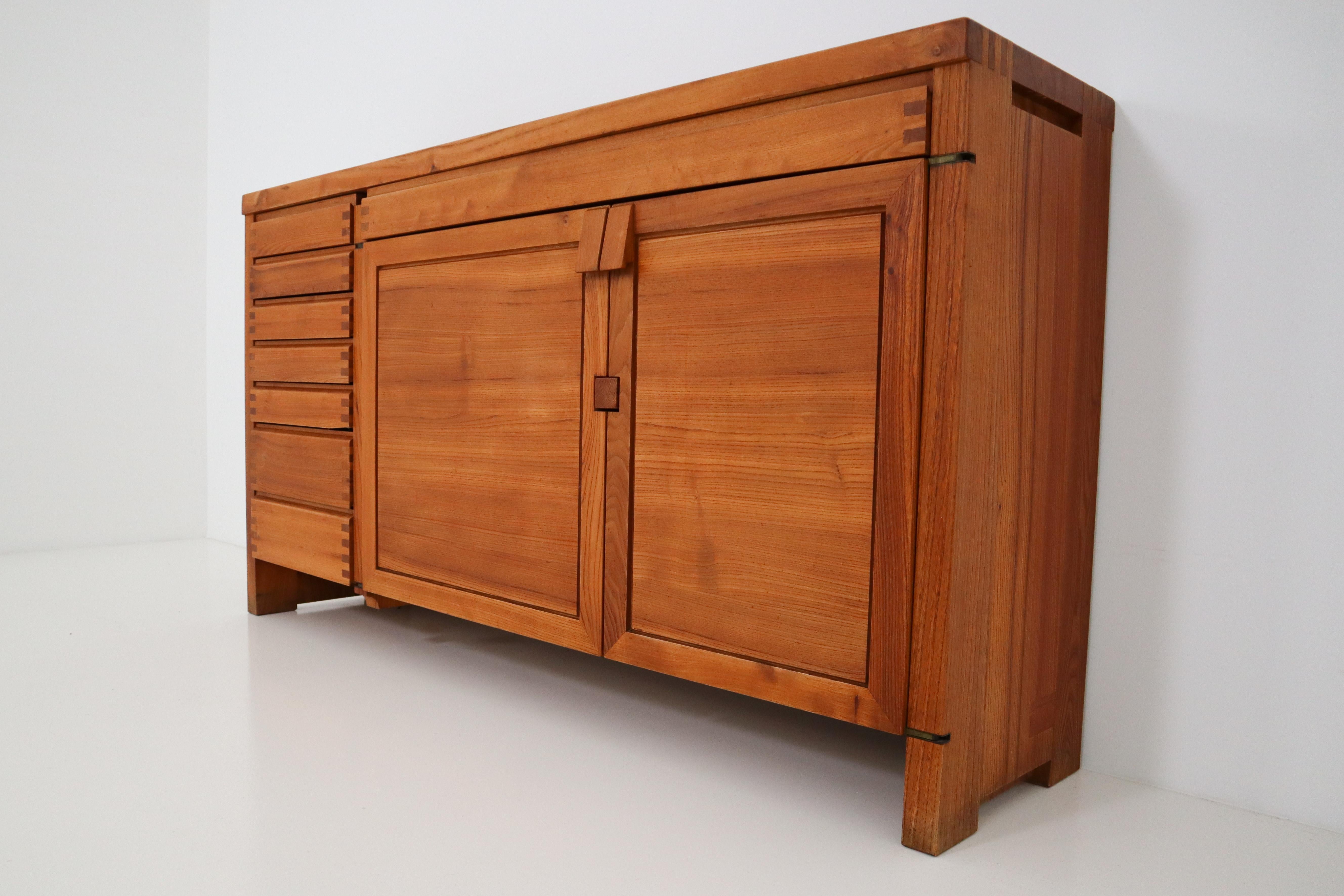 A large Pierre Chapo model R13 freestanding sideboard made of elm. This sideboard has two doors with triangle shaped knobs. The doors are locked by clamping them on the wooden block between them. There are seven smaller drawers and one large drawer