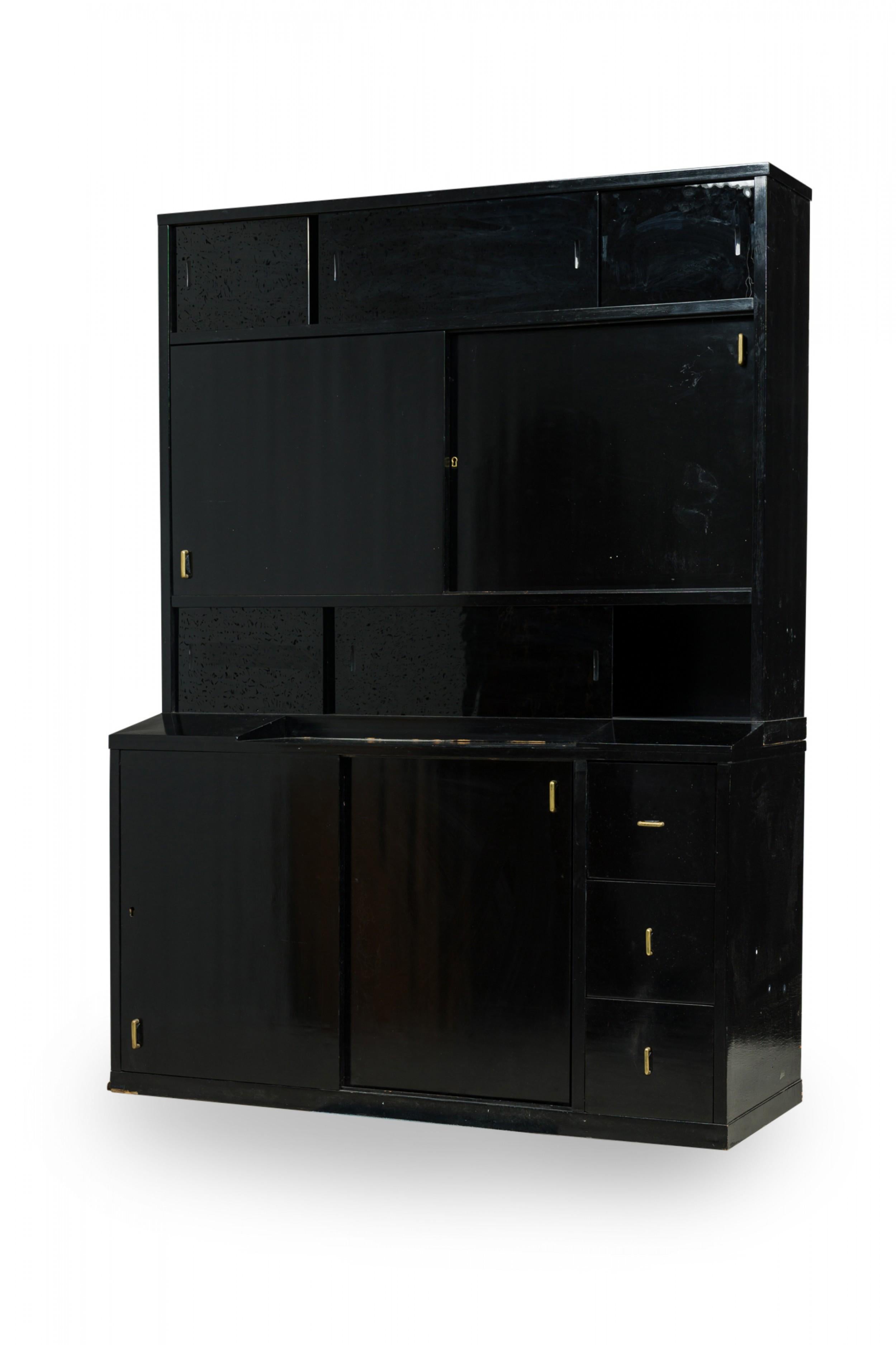 French Art Deco (1925) ebonized two-piece cabinet with the bottom section containing two large sliding doors flanked on the right by three smaller drawers and the top section having central sliding door compartment with black glass sliding door