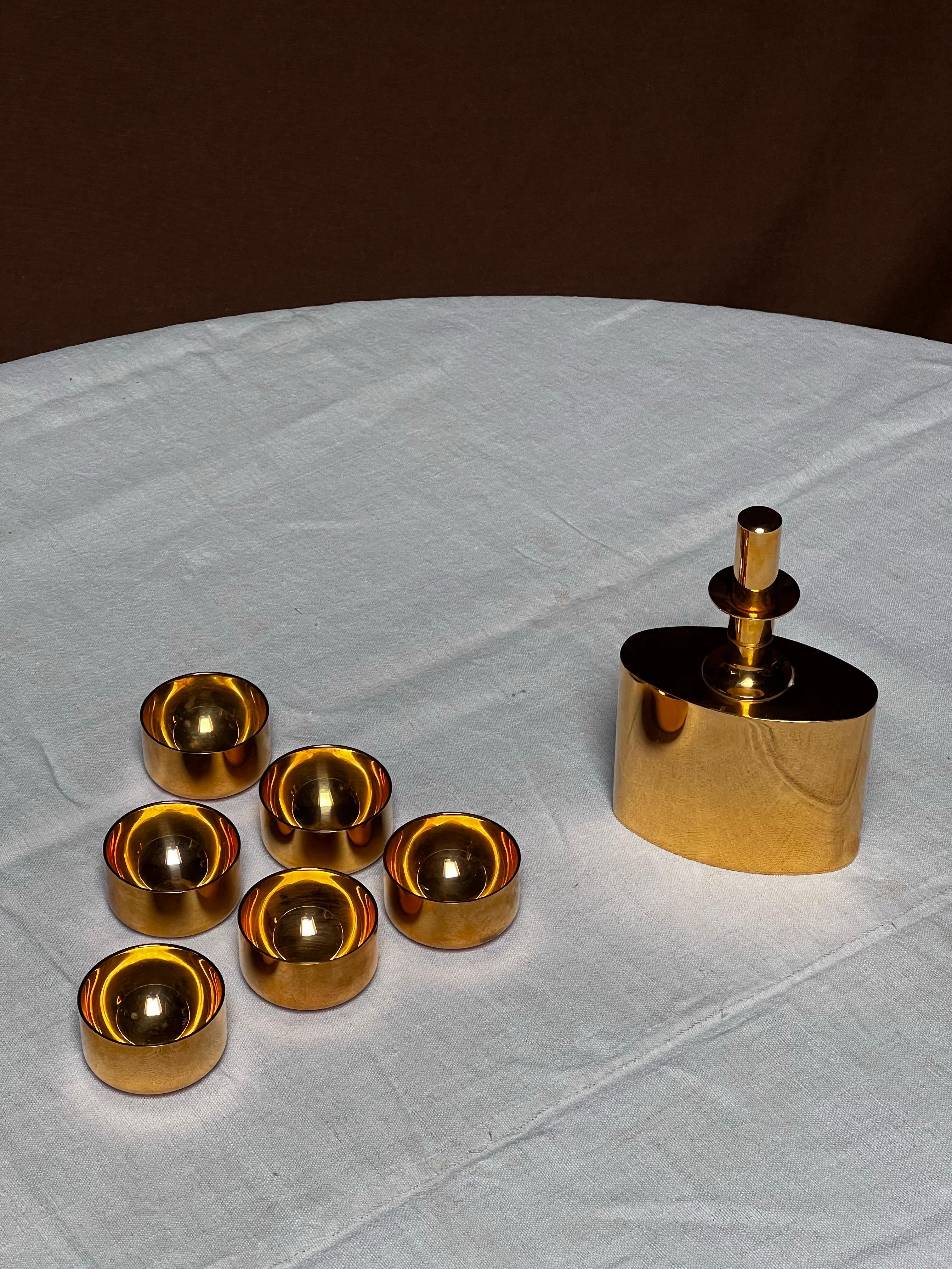 Questa serie di tazze e la relativa fiaschetta/caraffa sono state realizzate a mano negli anni '70 nella fabbrica di Skultuna, accanto allo studio in cui Pierre Forssell lavorava con il suo assistente. Sono realizzati in ottone e placcati in oro per