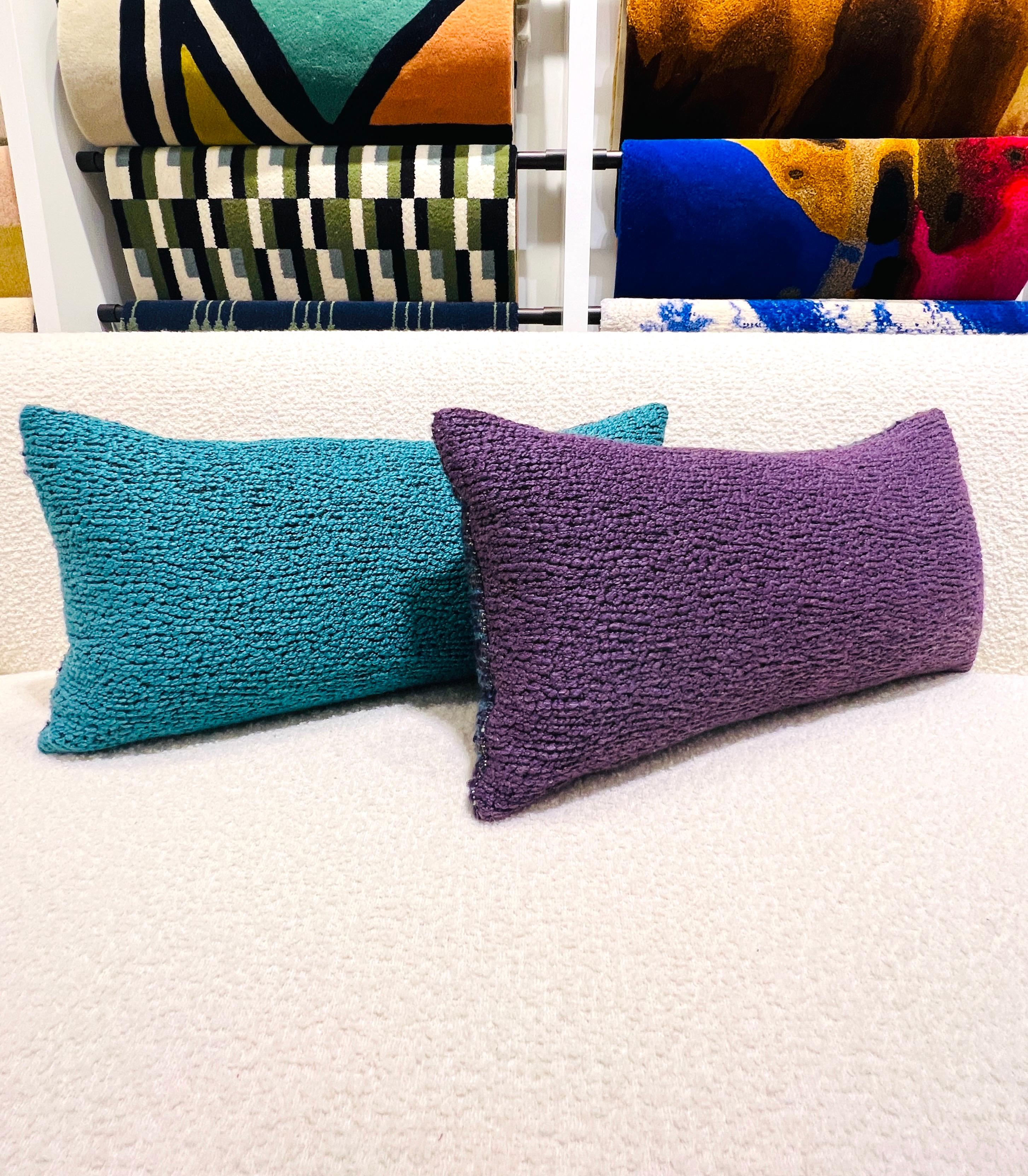 Pair of custom made throw pillows upholstered in Pierre Frey's Esteban fabric featuring textured wool-like threads which plays with the rustic codes of traditional Latin American weaves. One pillow in violet-purple, the other in turquoise-aqua, and