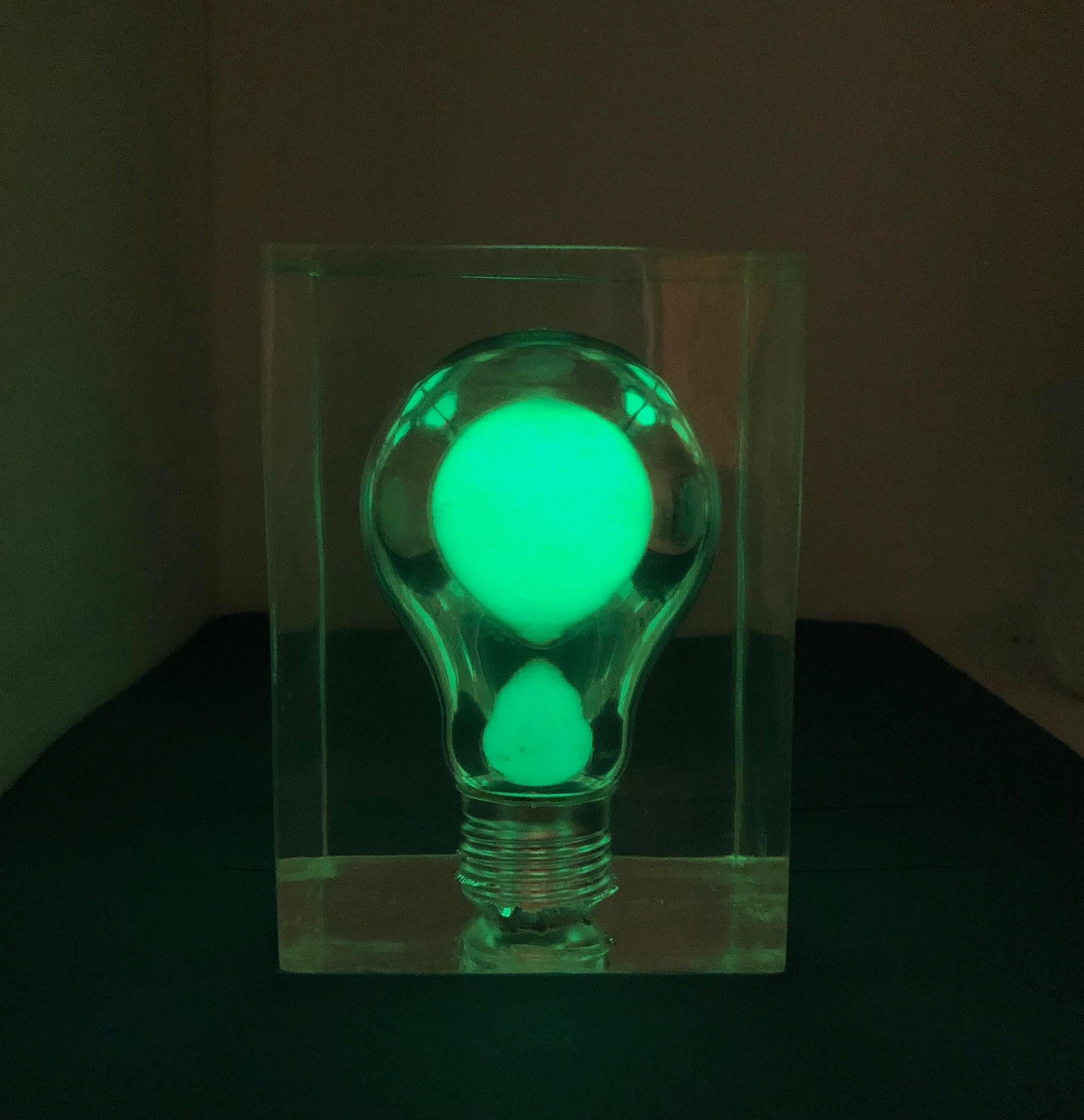This small but amazing French Pierre Giraudon haunting pop art Lucite light bulb sculpture glows in the dark. It lights up green inside in the dark and has the appearance of a light bulb floating in mid air. The phosphorescent bulb is encased in