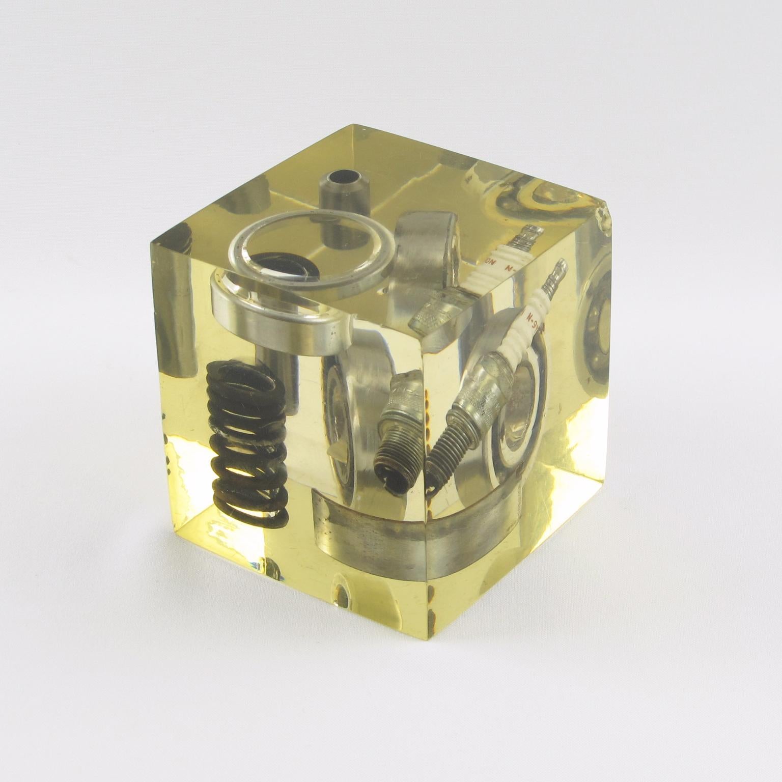 The design of this cube sculpture or resin paperweight is attributed to the French artist Pierre Giraudon. The resin cube features old industrial elements of an automobile engine. Car gears fit into layered cast resin. A natural yellowish coloring