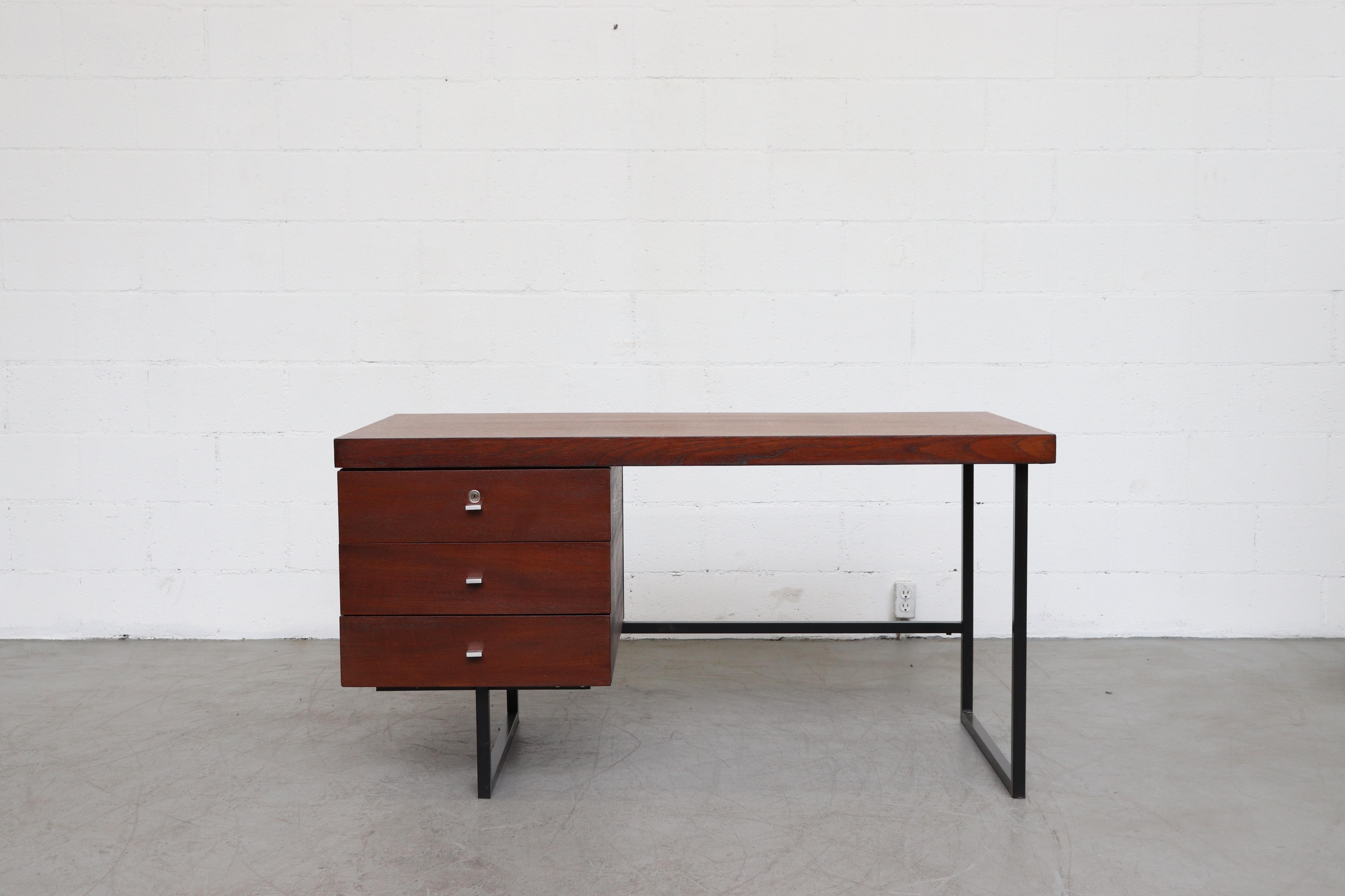 Pierre Guariche dark teak writing desk. Three stacked drawers and black enameled metal base frame. In original condition with visible signs of visual wear consistent with age and use. No key available.