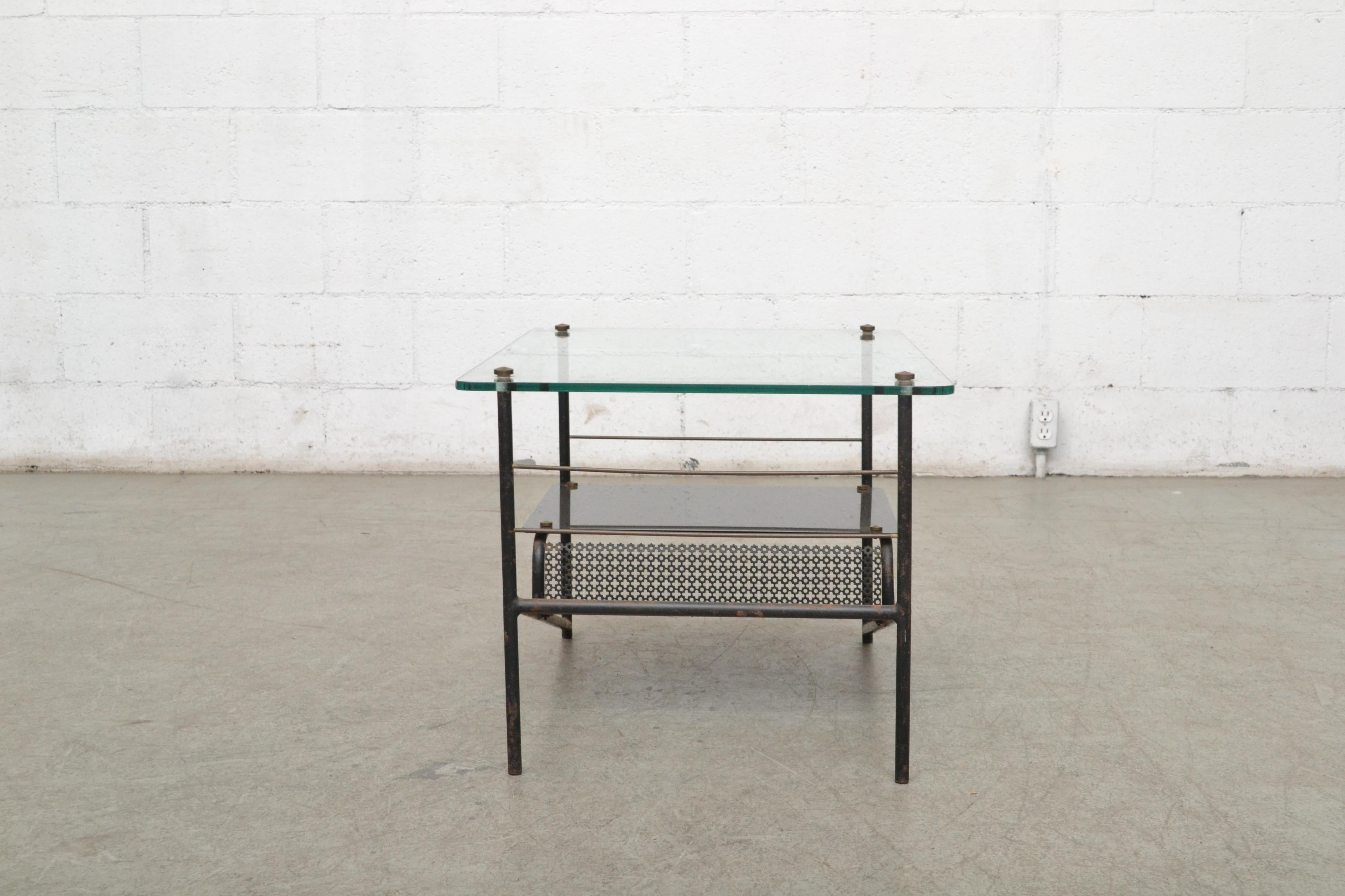 Pierre Guariche and Mathieu Matégot inspired mid-century side table with plate glass top, perforated magazine rack. Black enameled metal frame. Visible wear consistent with age and usage. Nice visible patina and some enamel loss.